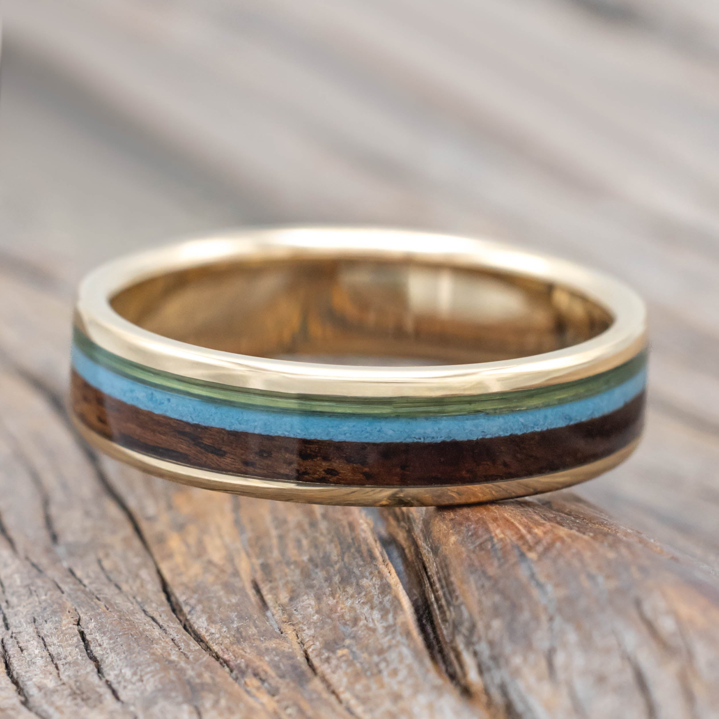 Yellow gold ring with fishing line, koa wood, and turquoise inlays on a wooden surface