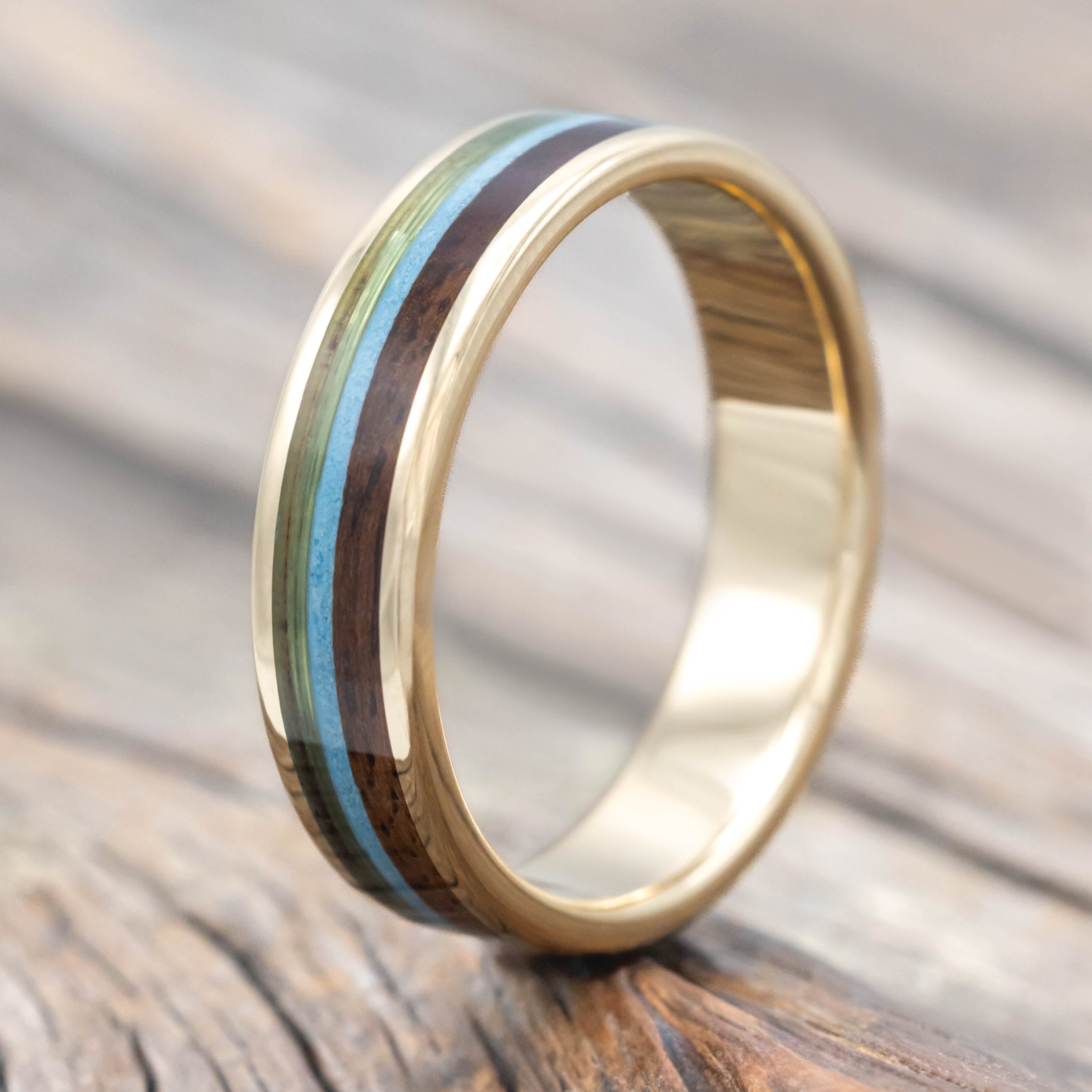 Yellow gold ring with fishing line, koa wood, and turquoise inlays on a wooden surface