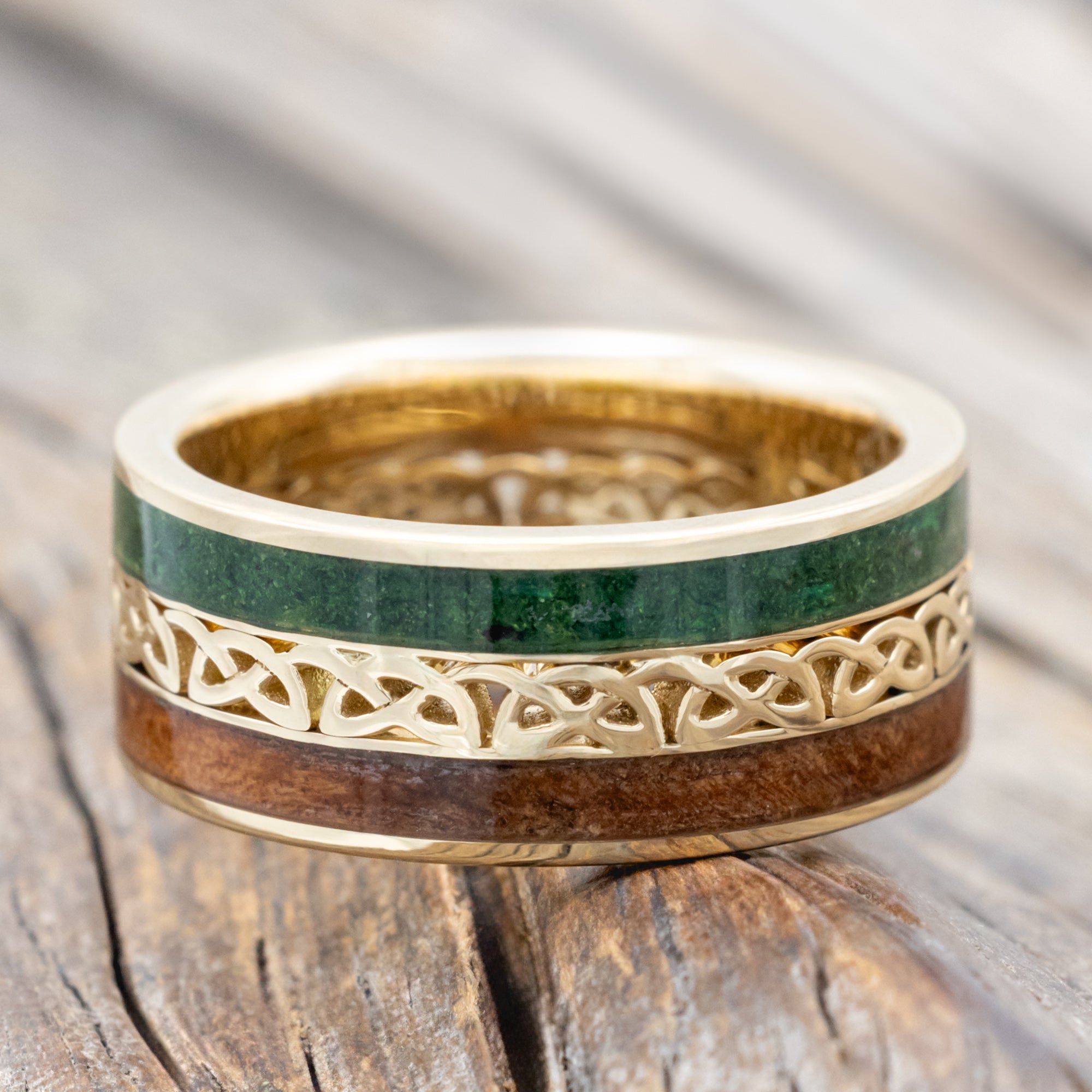 Gold ring with moss and redwood inlays with Celtic cutout on a wooden surface
