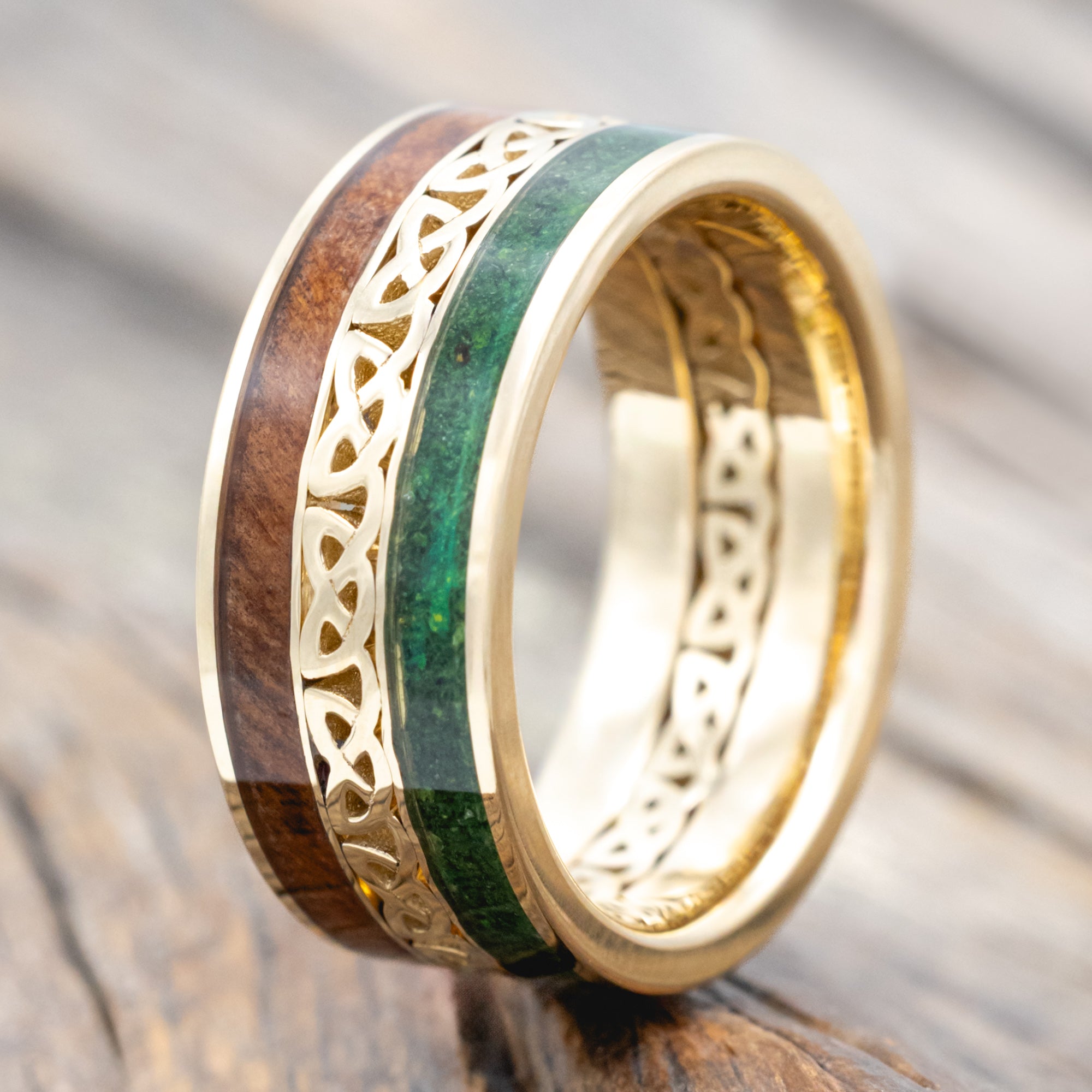 Gold ring with moss and redwood inlays with Celtic cutout on a wooden surface