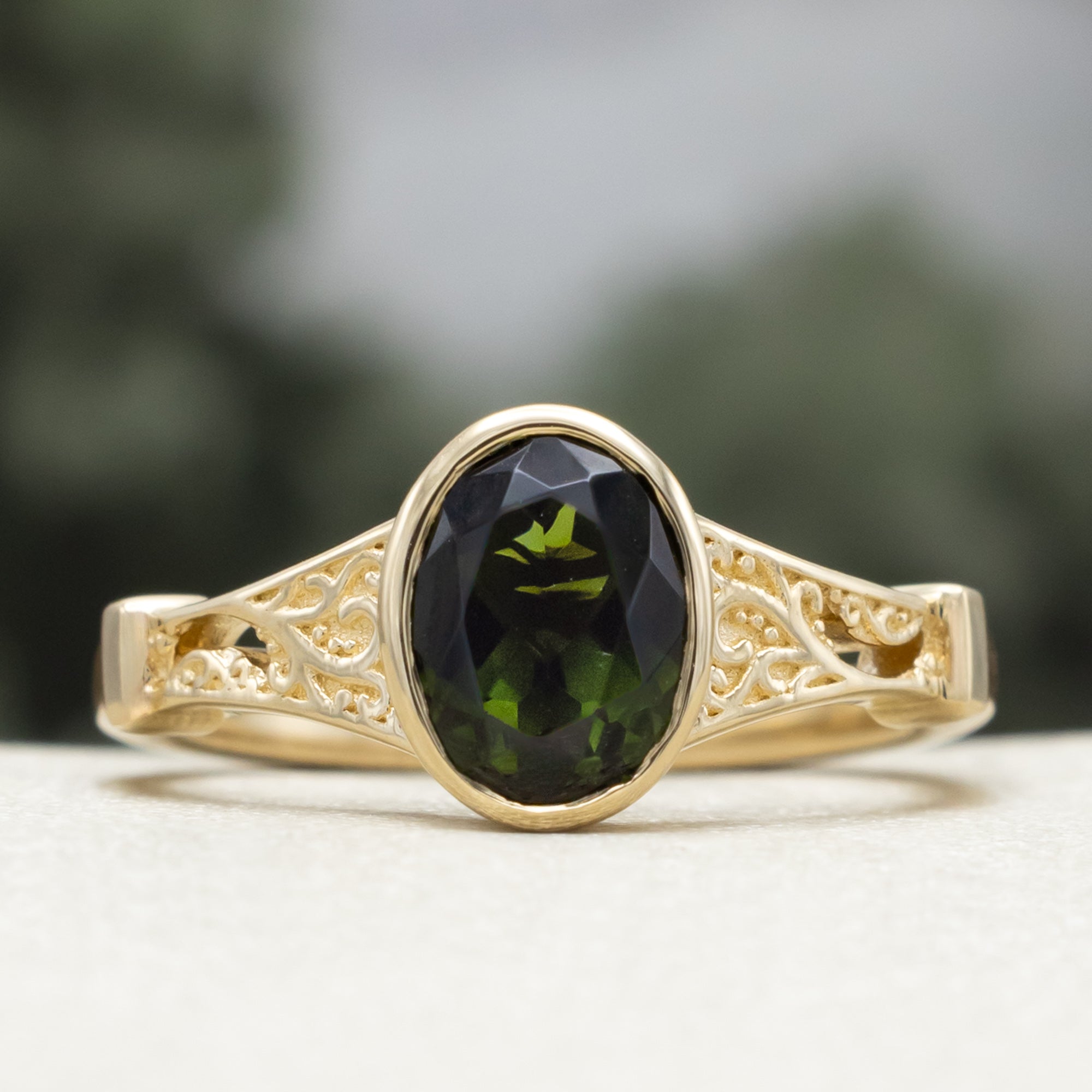 Gold ring with oval cut green tourmaline against a blurred green background