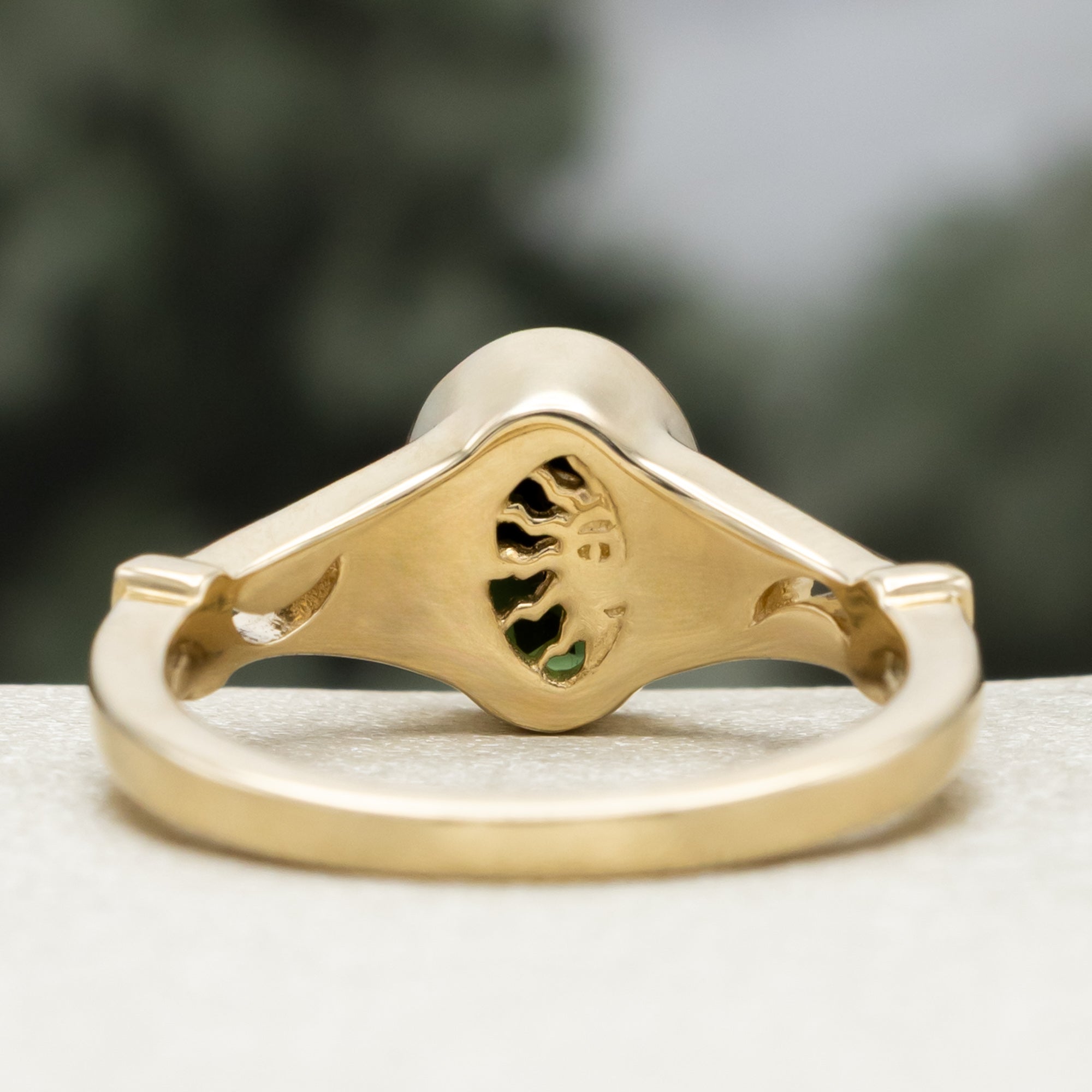 Gold ring with oval cut green tourmaline against a blurred green background