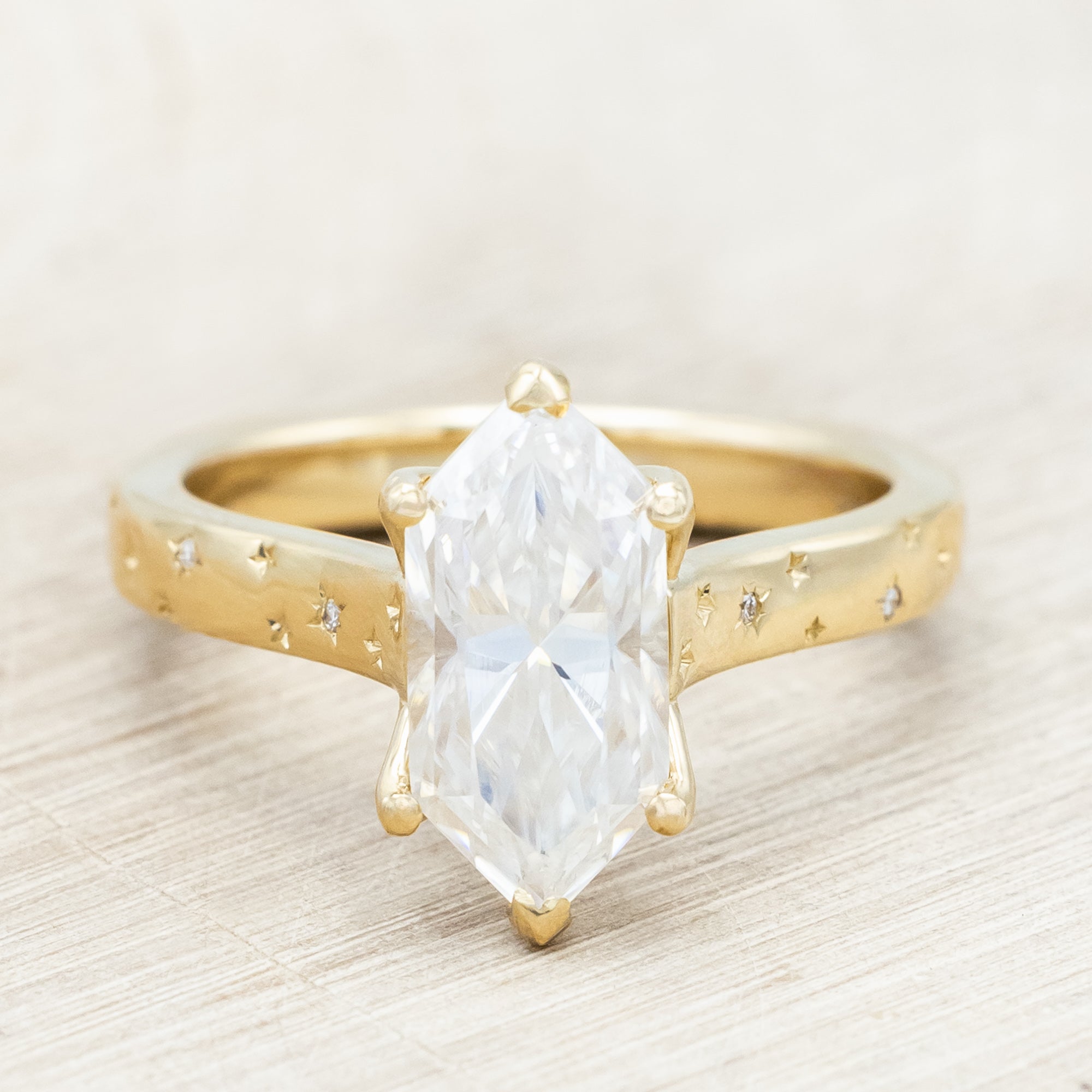 Gold ring with a moissanite center stone on a wooden stand against a neutral background