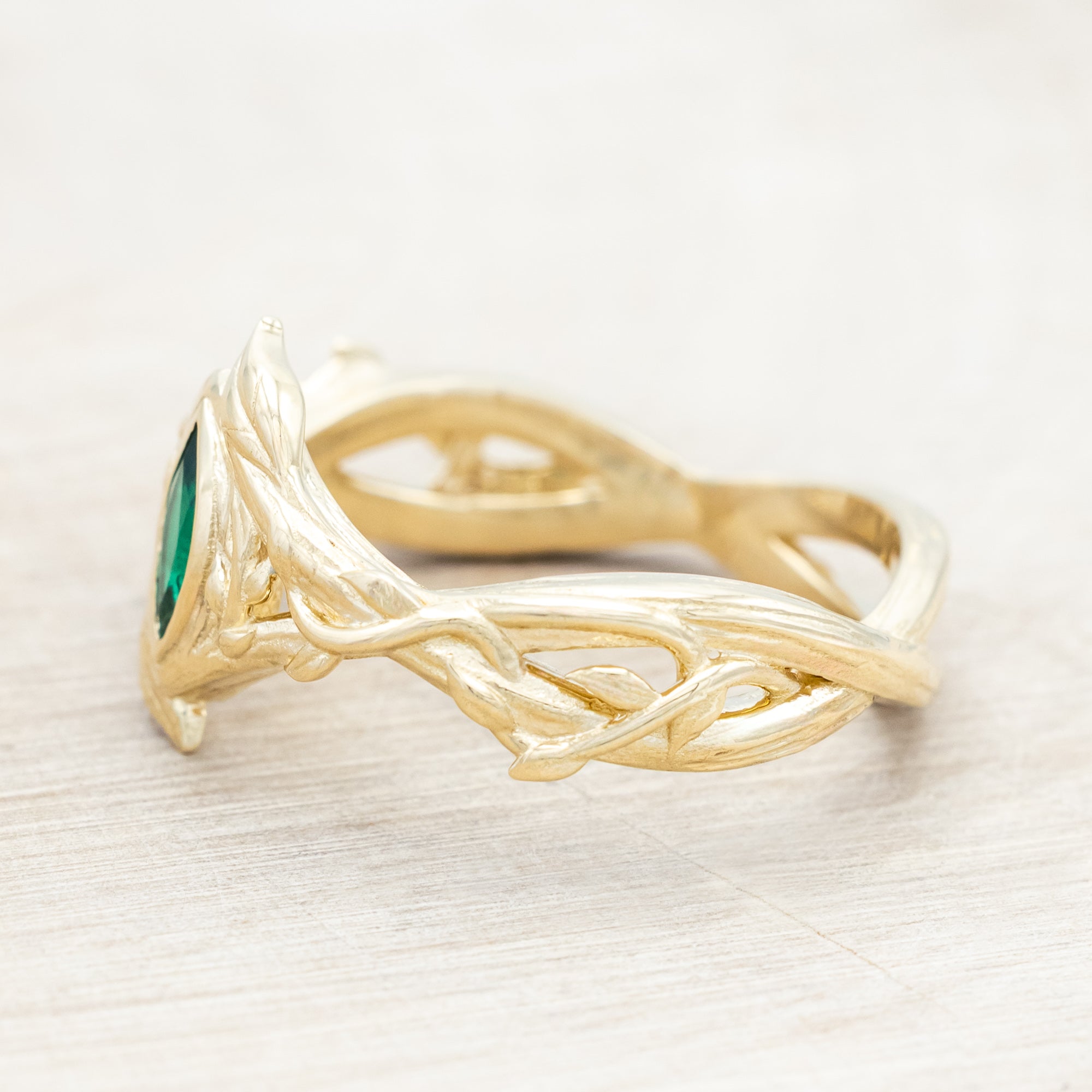 Gold ring with a green lab emerald against a light wooden background