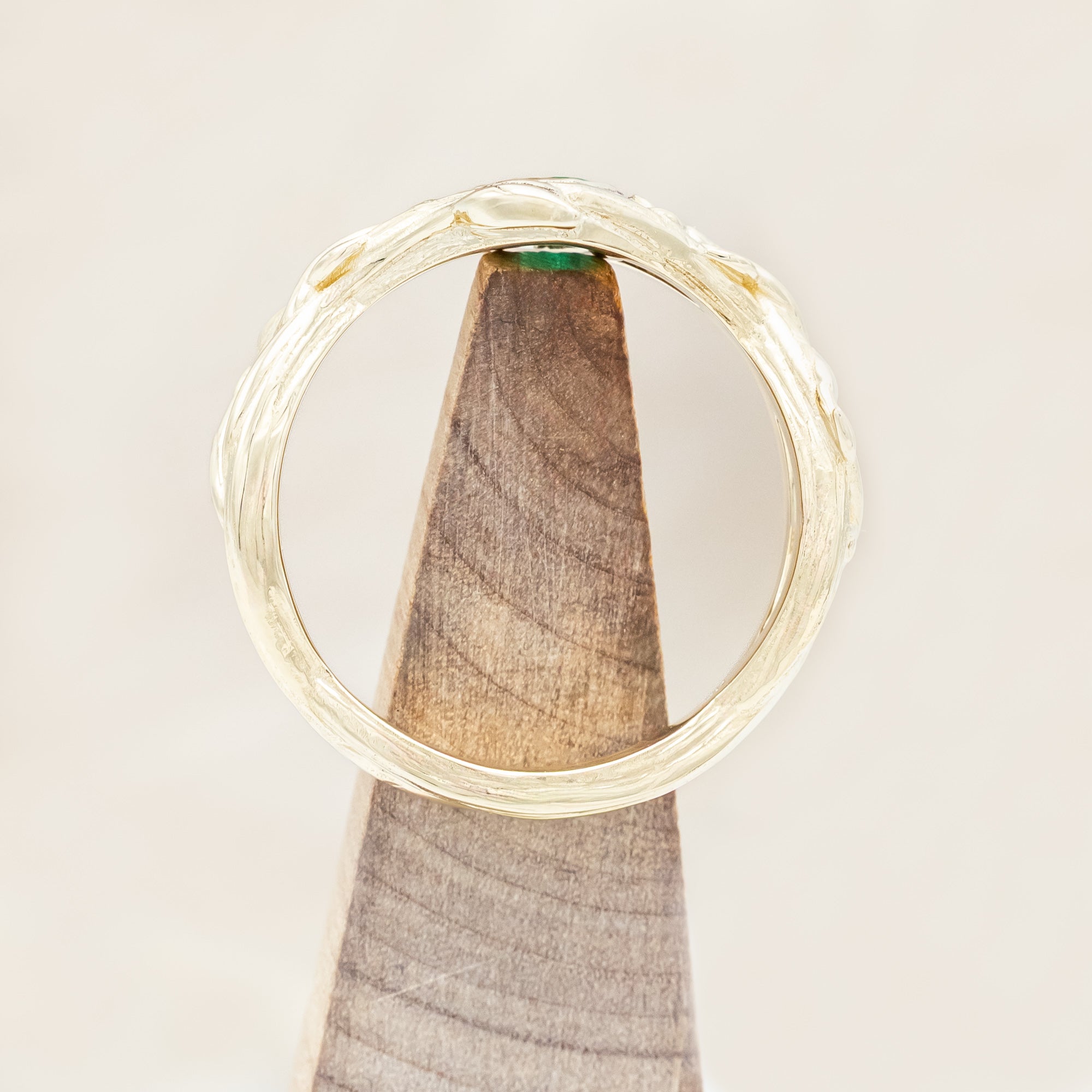 Gold ring with a green lab emerald against a light wooden background