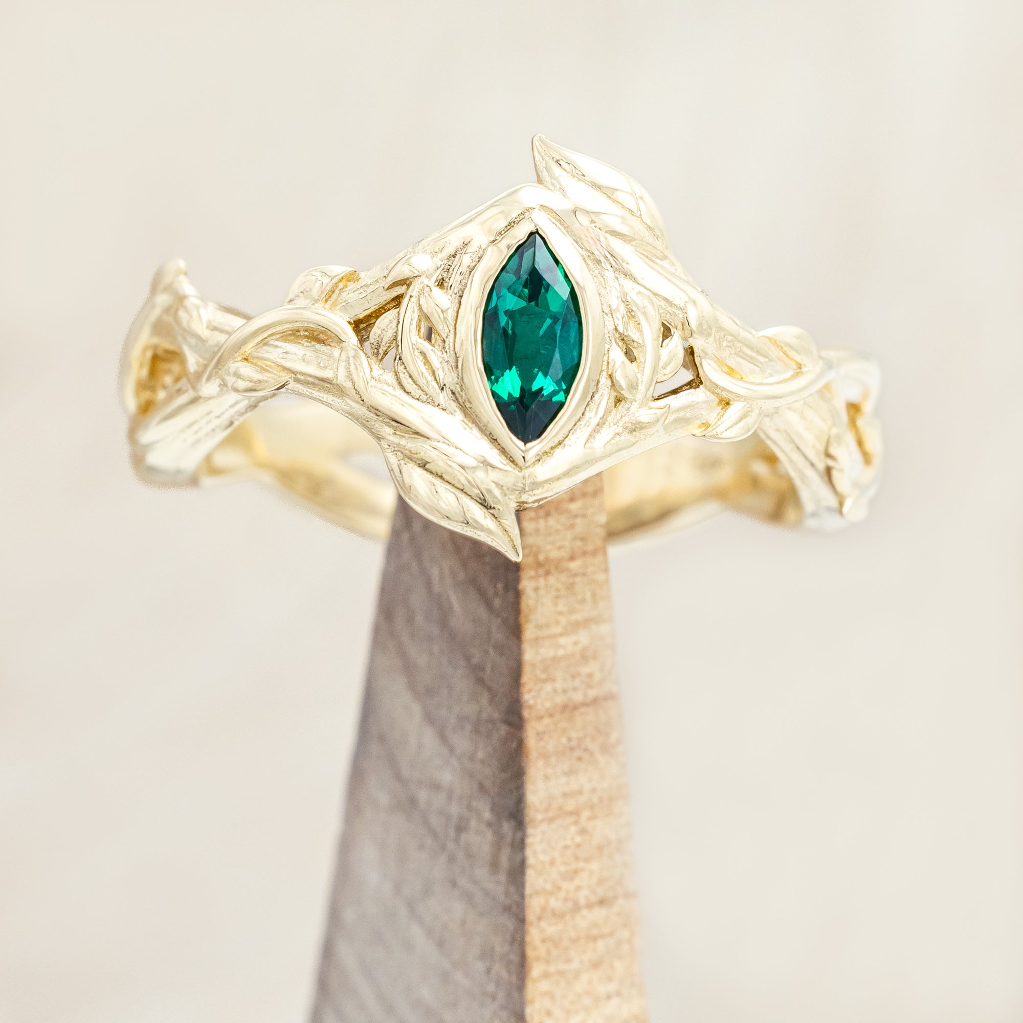 Gold ring with a green lab emerald on a wooden stand against a beige background