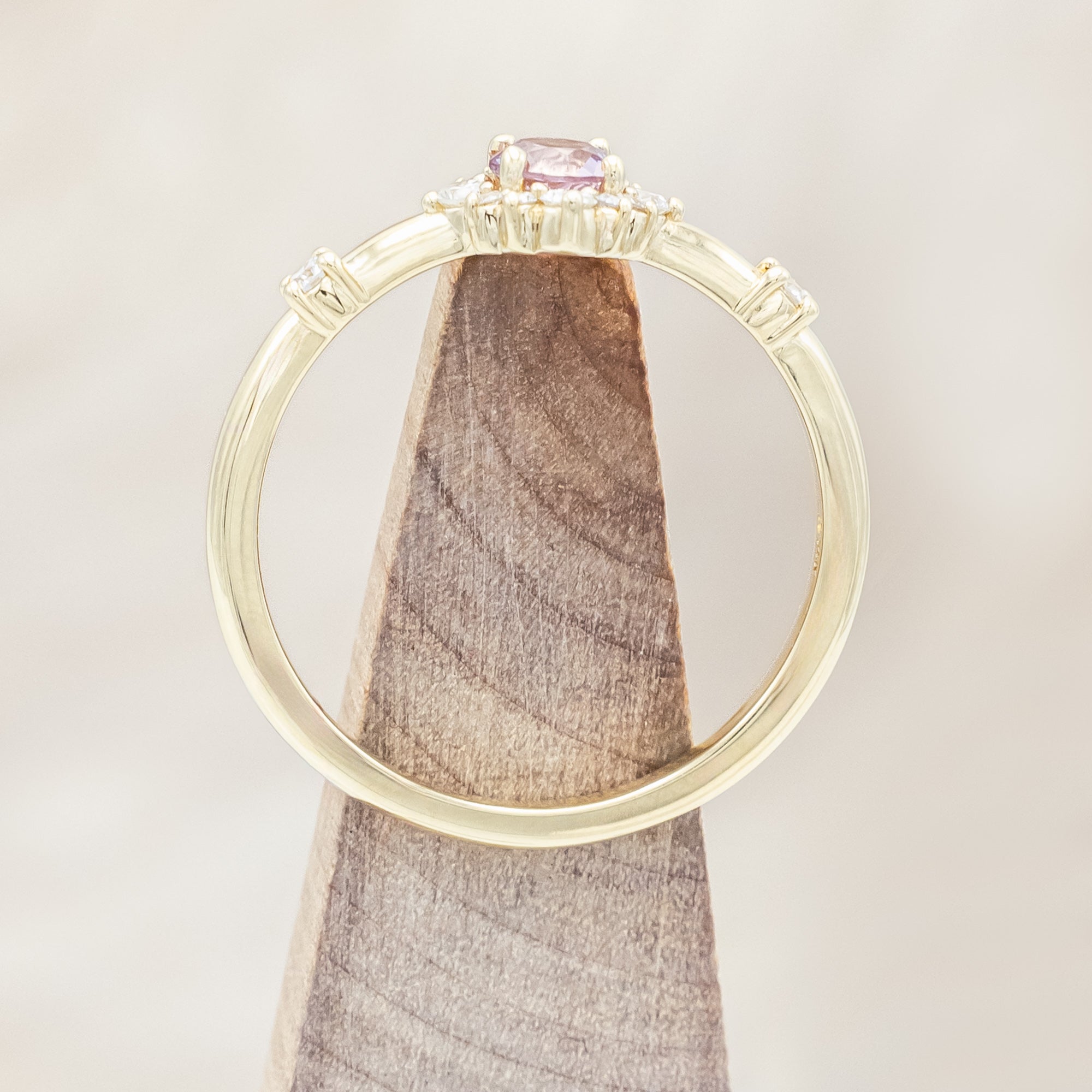 Gold ring with a dragon garnet and diamond accents on a wooden stand against a beige background