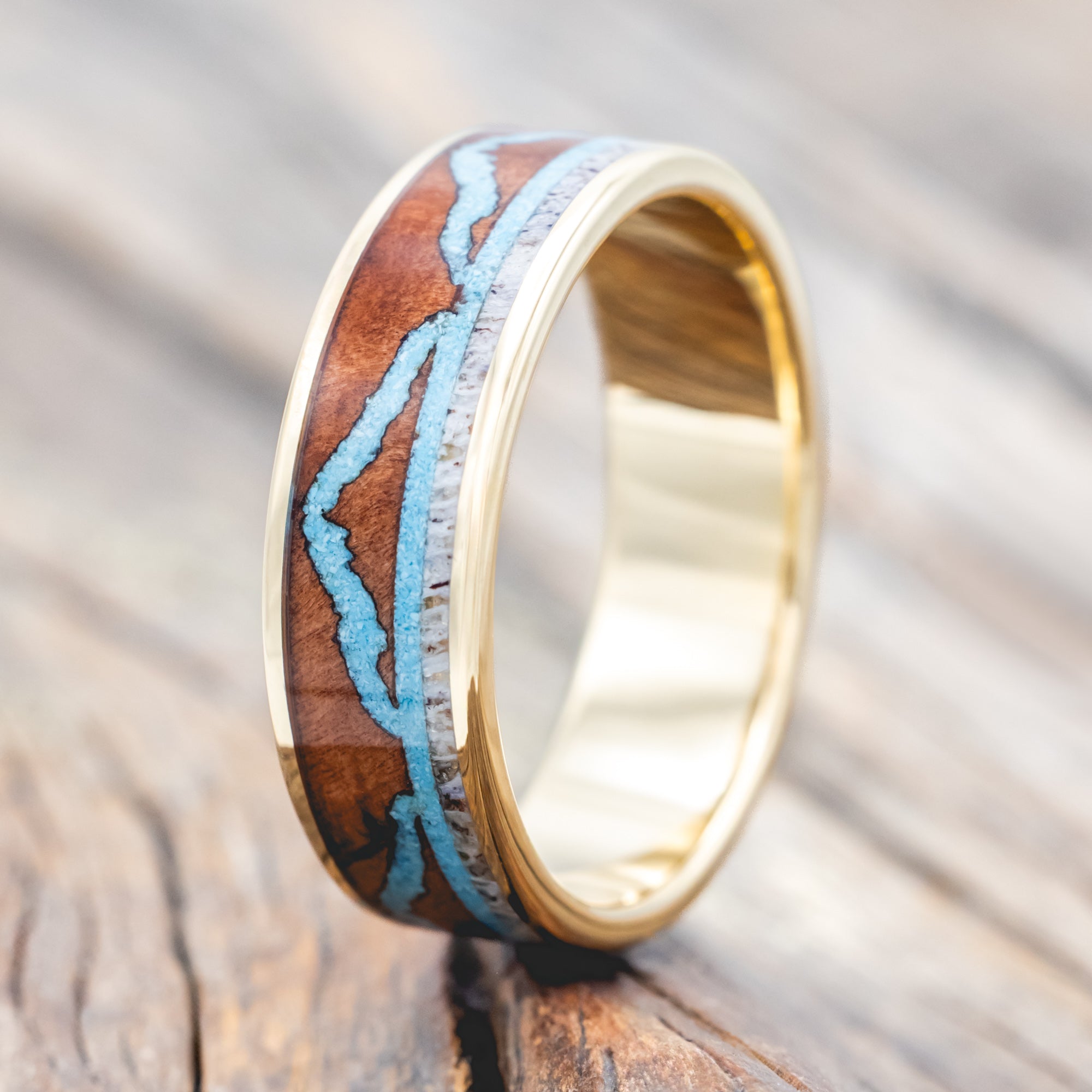 Yellow gold ring with whiskey barrel, antler, and turquoise mountains on a wooden surface