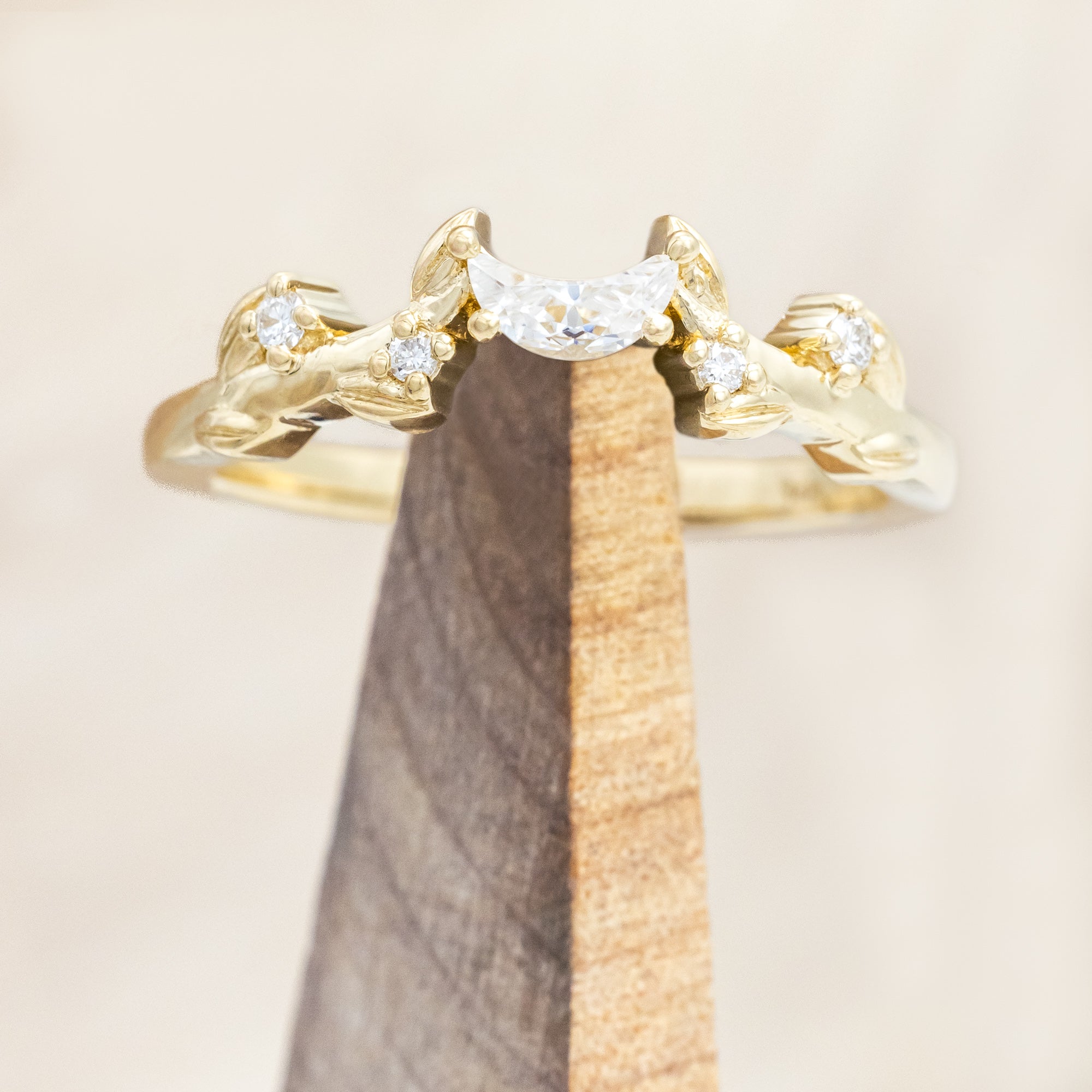 14K gold ring with diamond & moissanite accents on a wooden stand against a beige background