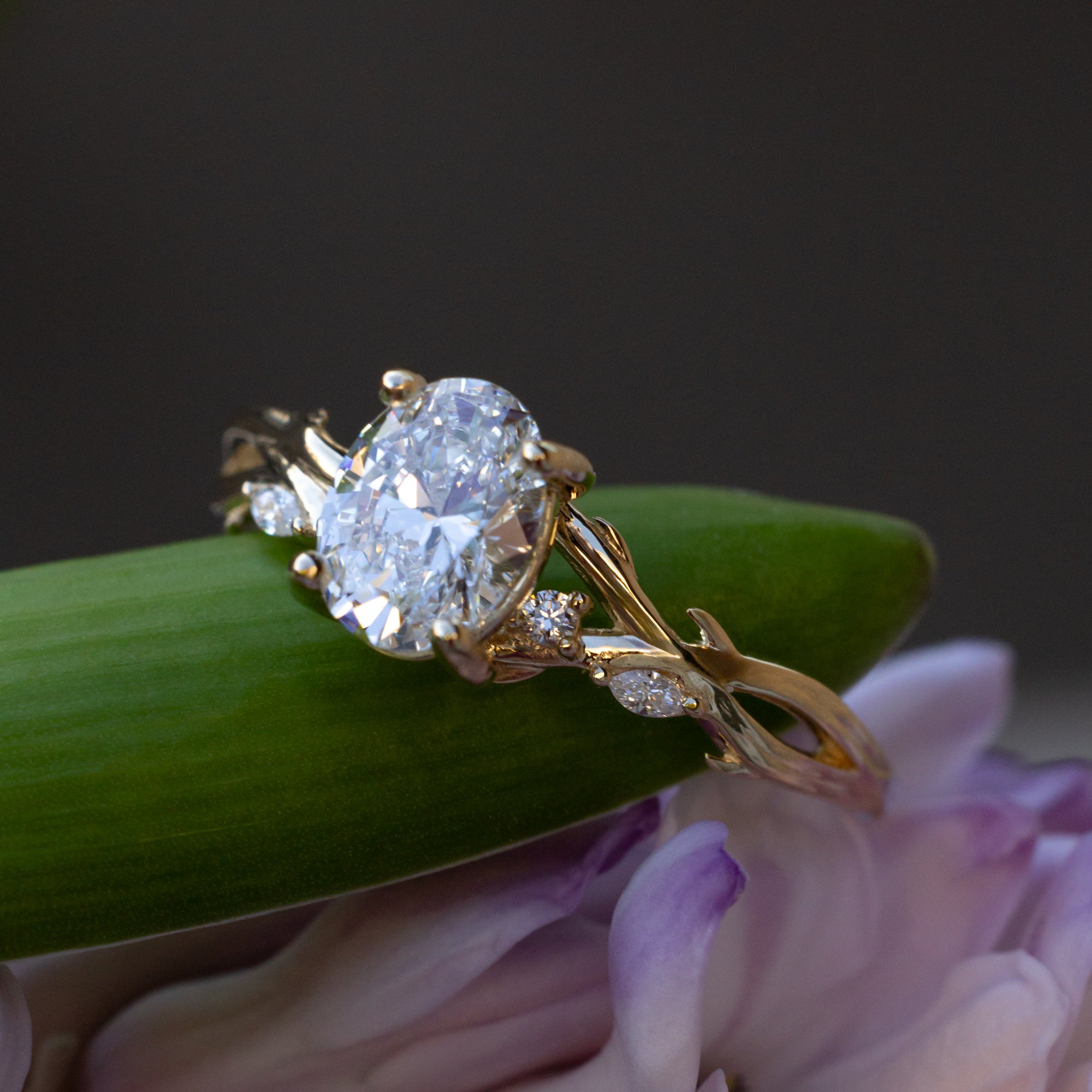 Gold ring with oval lab diamond center stone with diamond accents against a blurred floral background