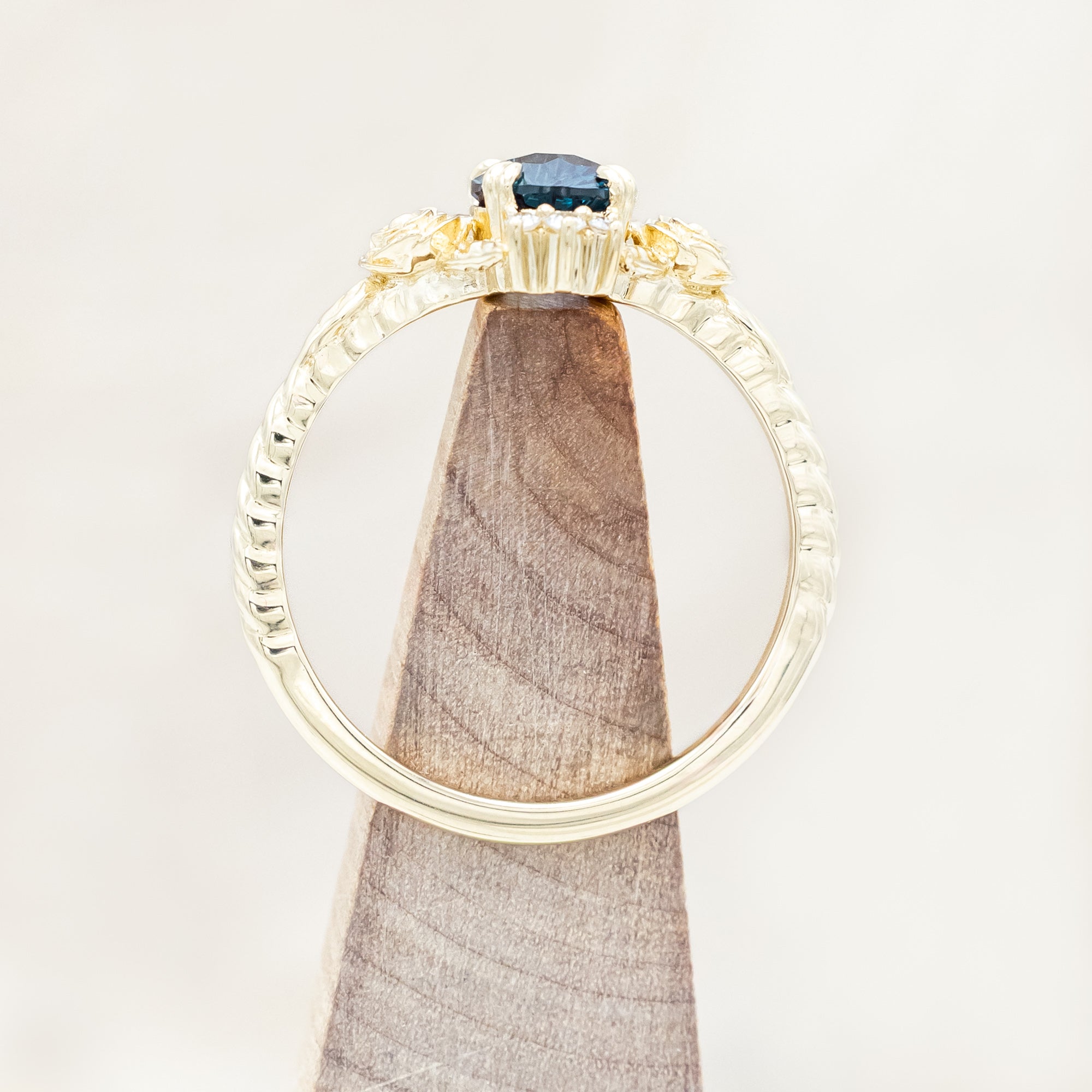 Yellow gold floral-inspired ring with lab alexandrite center stone and diamond accents on a light wooden background