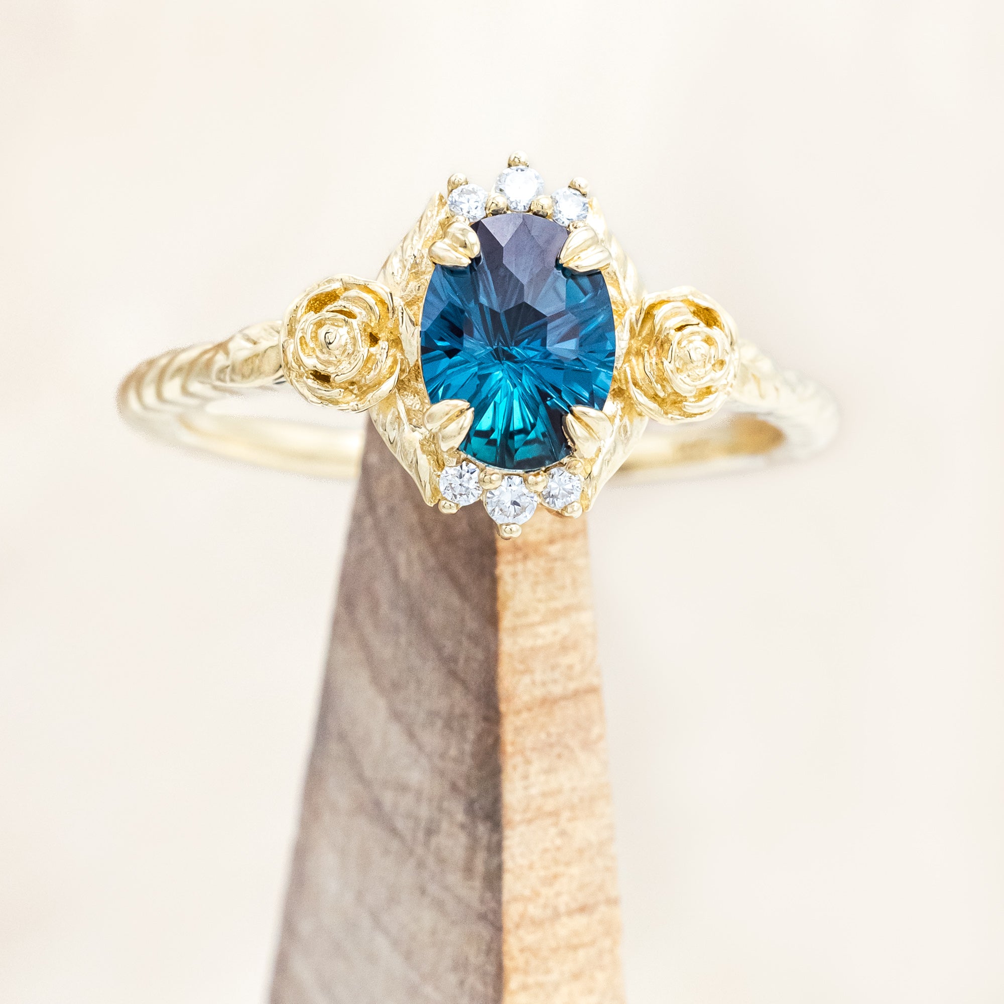 Yellow gold floral-inspired ring with lab alexandrite center stone and diamond accents on a wooden stand