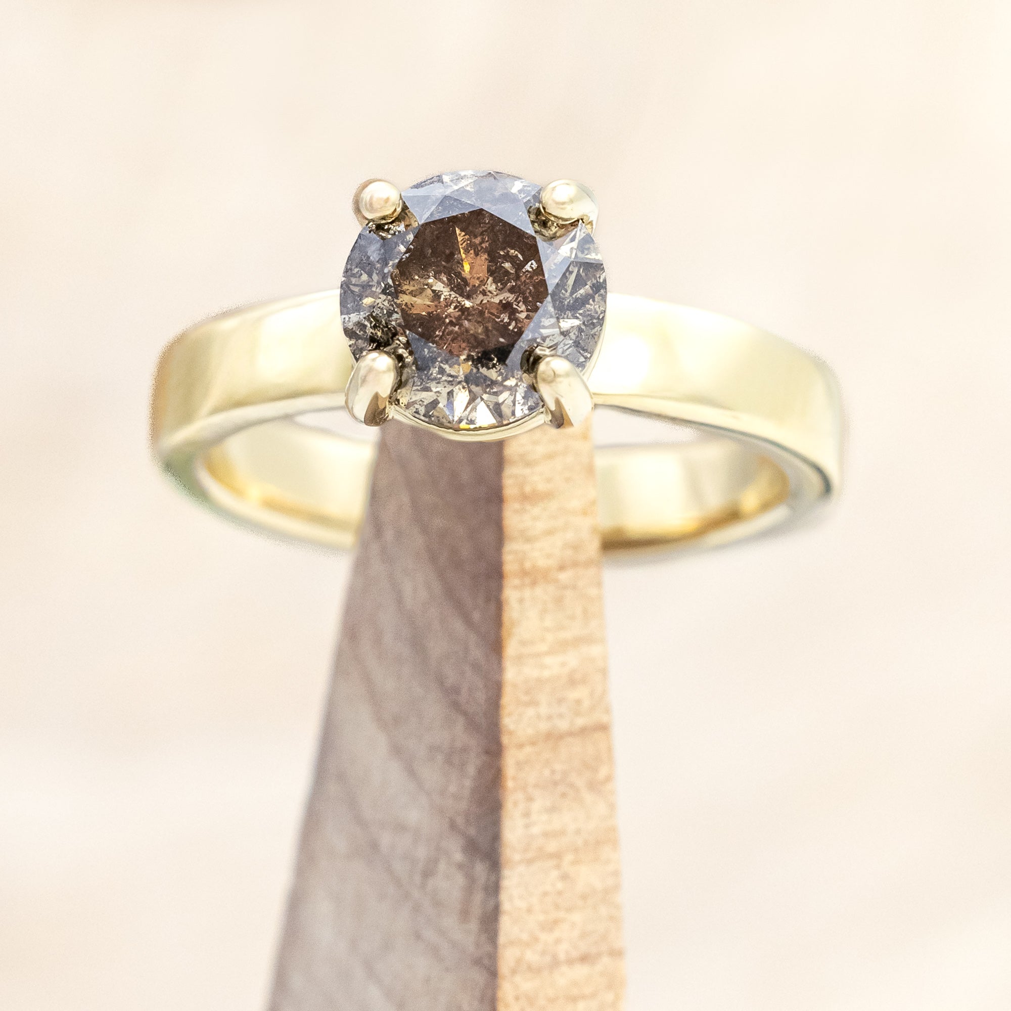 Wide 14K gold ring with a salt & pepper diamond on a beige background