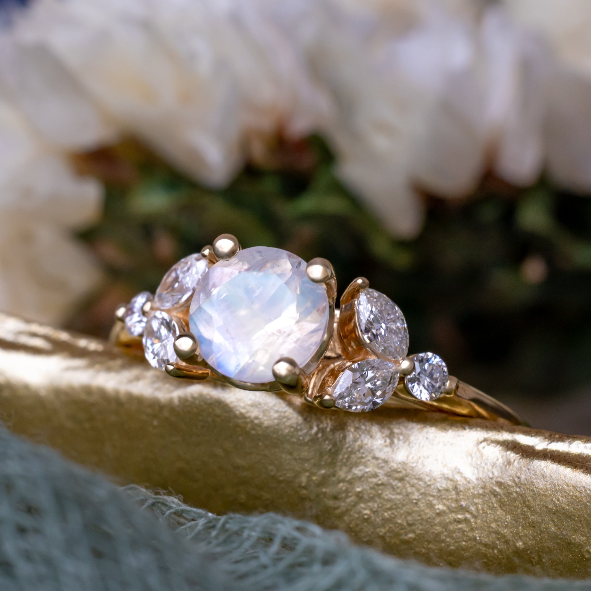 Gold engagement ring with moonstone and diamond accents on a textured surface