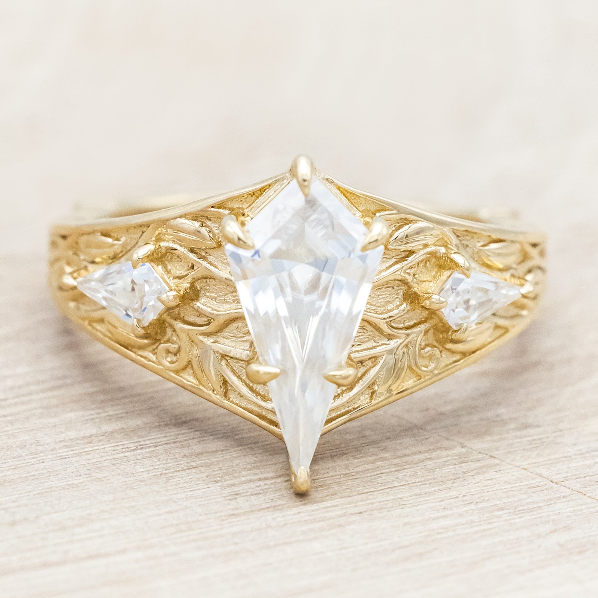 14K yellow gold ring with kite cut Moissanite and two smaller Moissanite accents on a light wooden background
