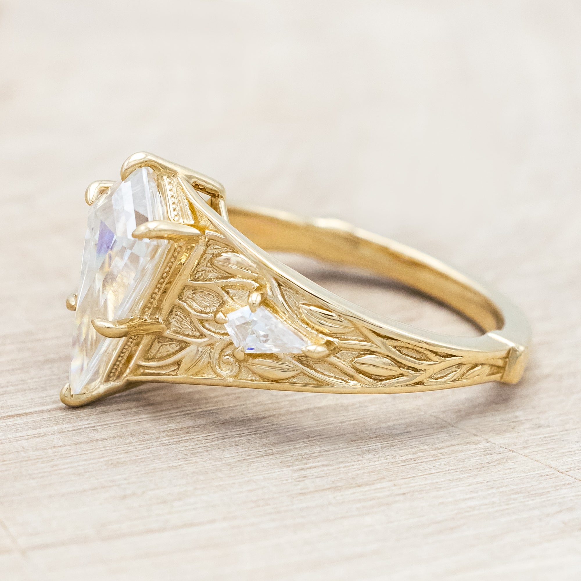 14K yellow gold ring with kite cut Moissanite and two smaller Moissanite accents on a light wooden surface