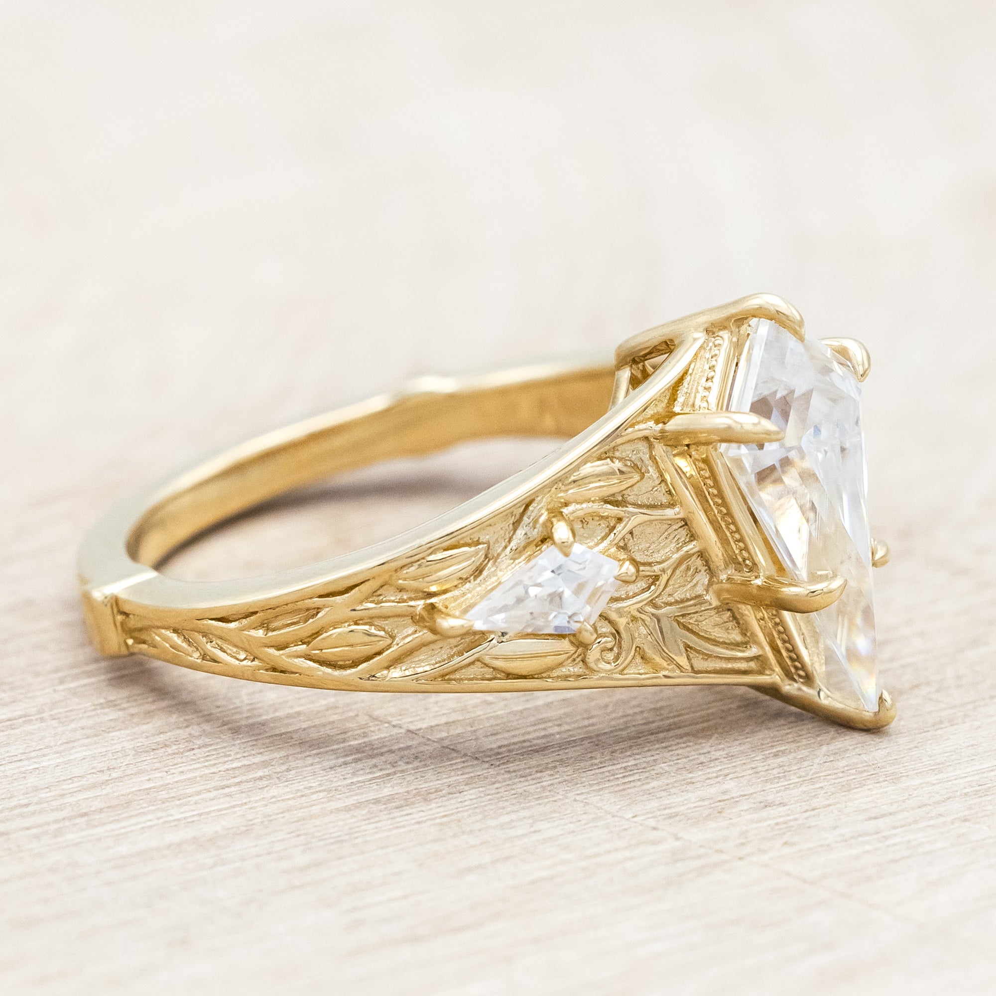 14K yellow gold ring with kite cut Moissanite and two smaller Moissanite accents on a light wooden surface