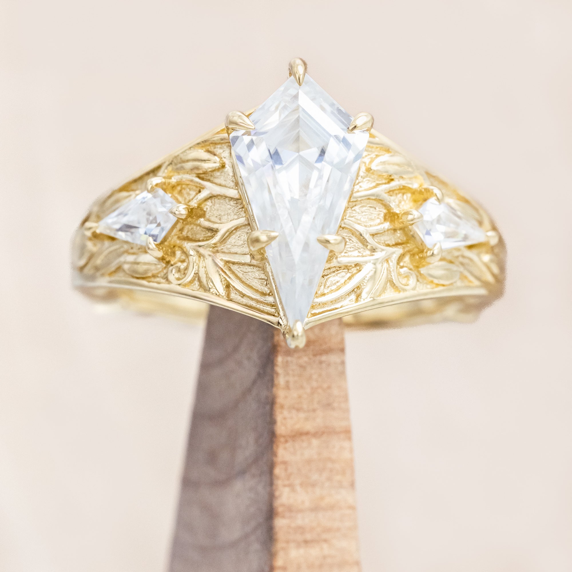 14K yellow gold ring with kite cut Moissanite and two smaller Moissanite accents on a beige background