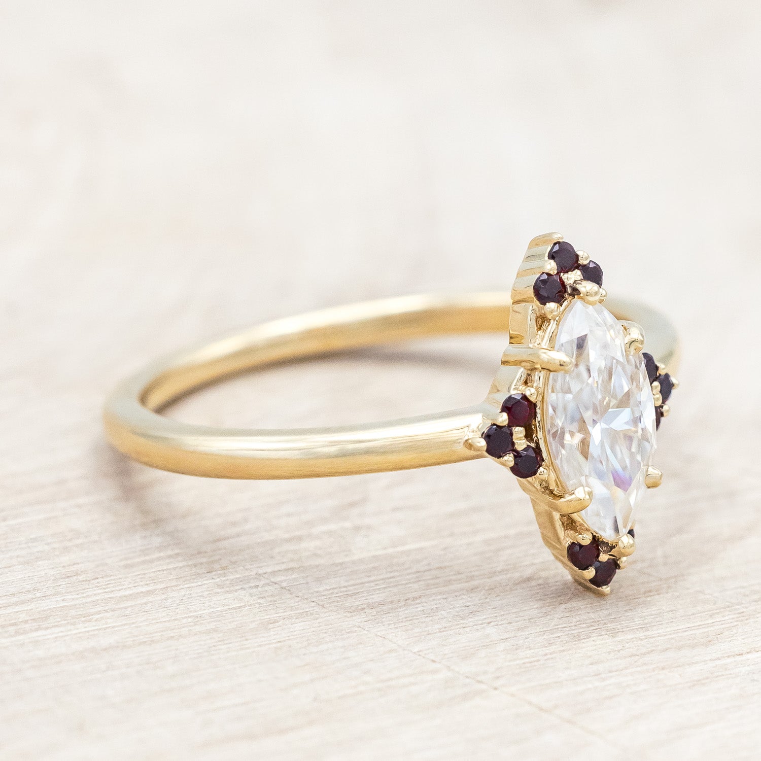 14K gold ring with Moissanite center stone and smaller red garnets on a light background