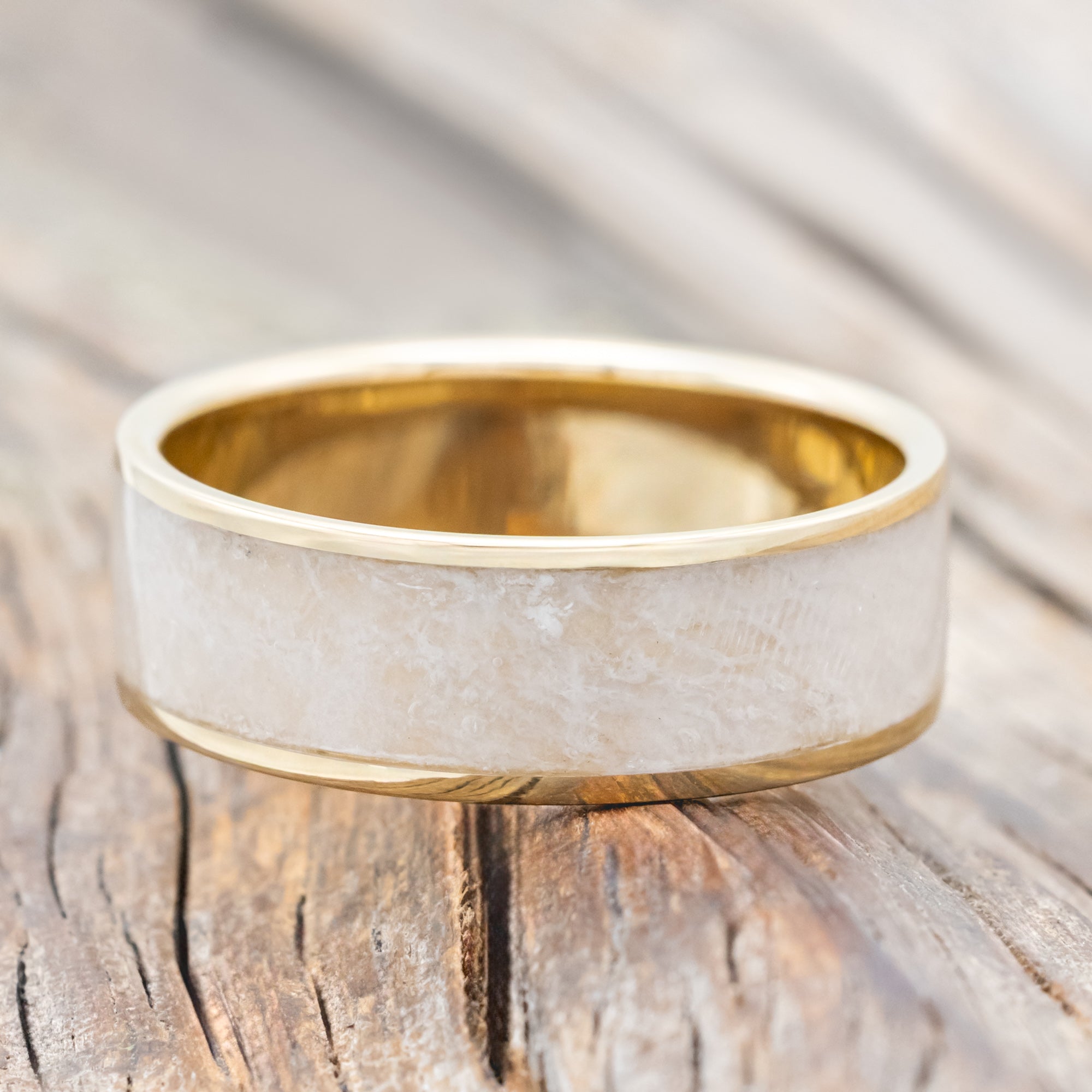 Gold ring with wedding dress inlay on a wooden surface