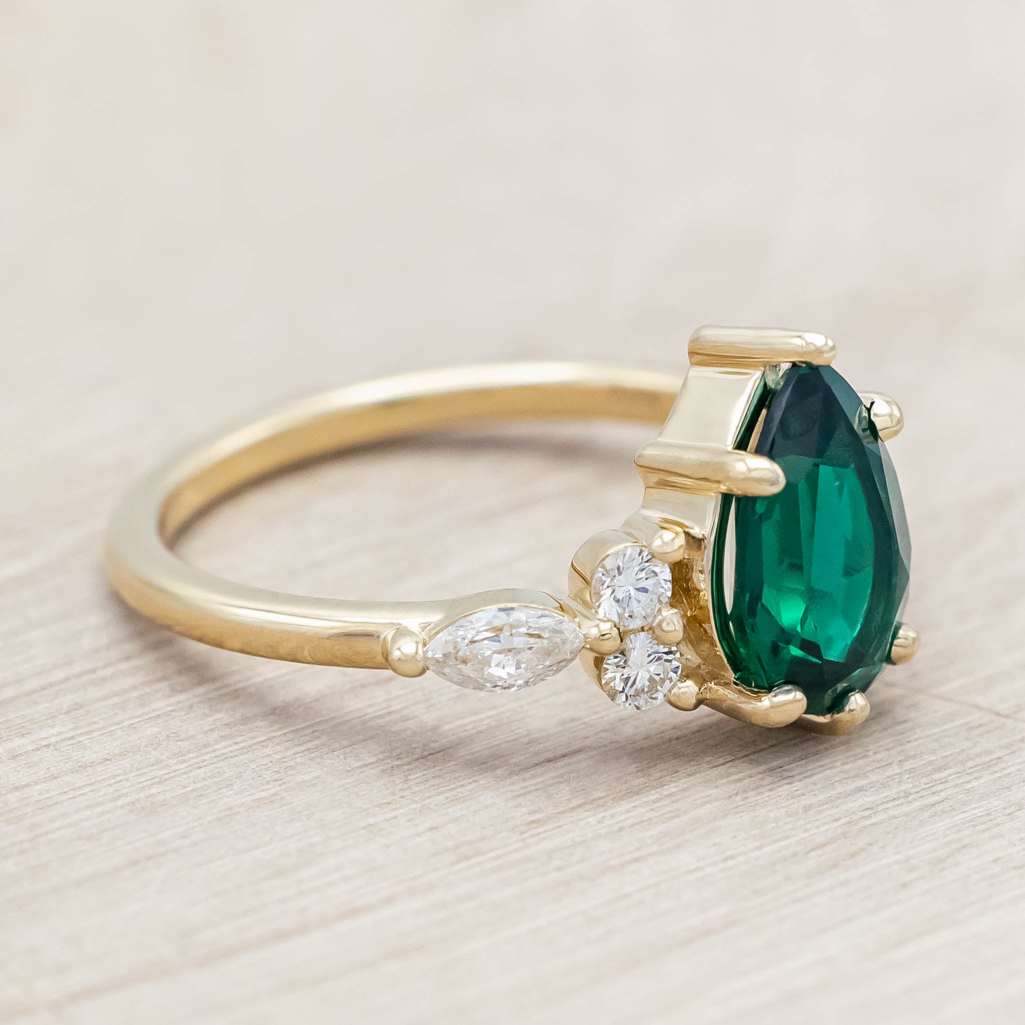 Gold ring with a green emerald and smaller diamond accents on a light wooden surface