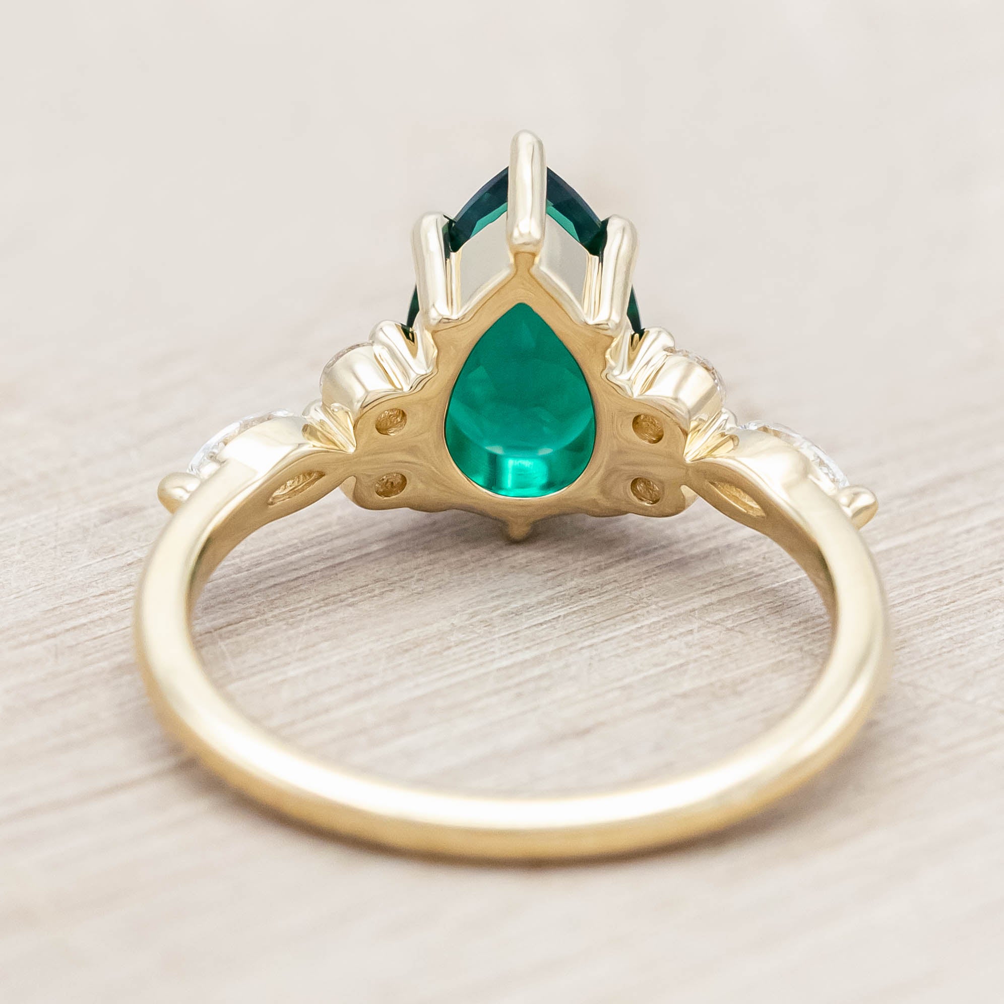 Gold ring with a green emerald and smaller diamond accents on a light wooden surface