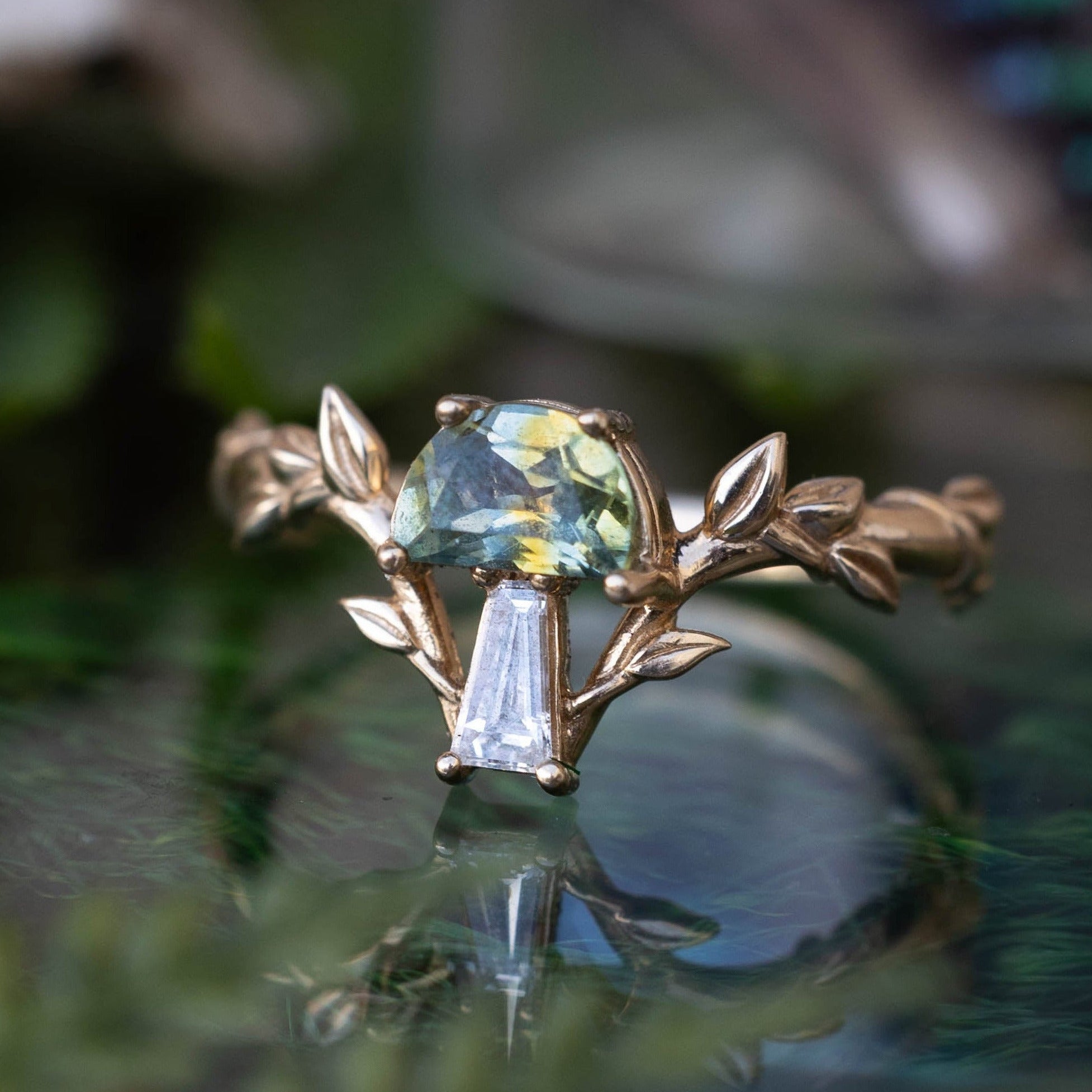 Gold ring with a green gemstone on a reflective surface with blurred natural background