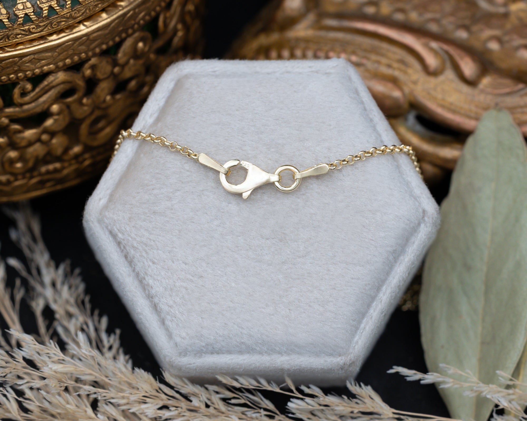 Back of gold chain with lobster clasp, sitting on a white cushion with dried flowers in the background