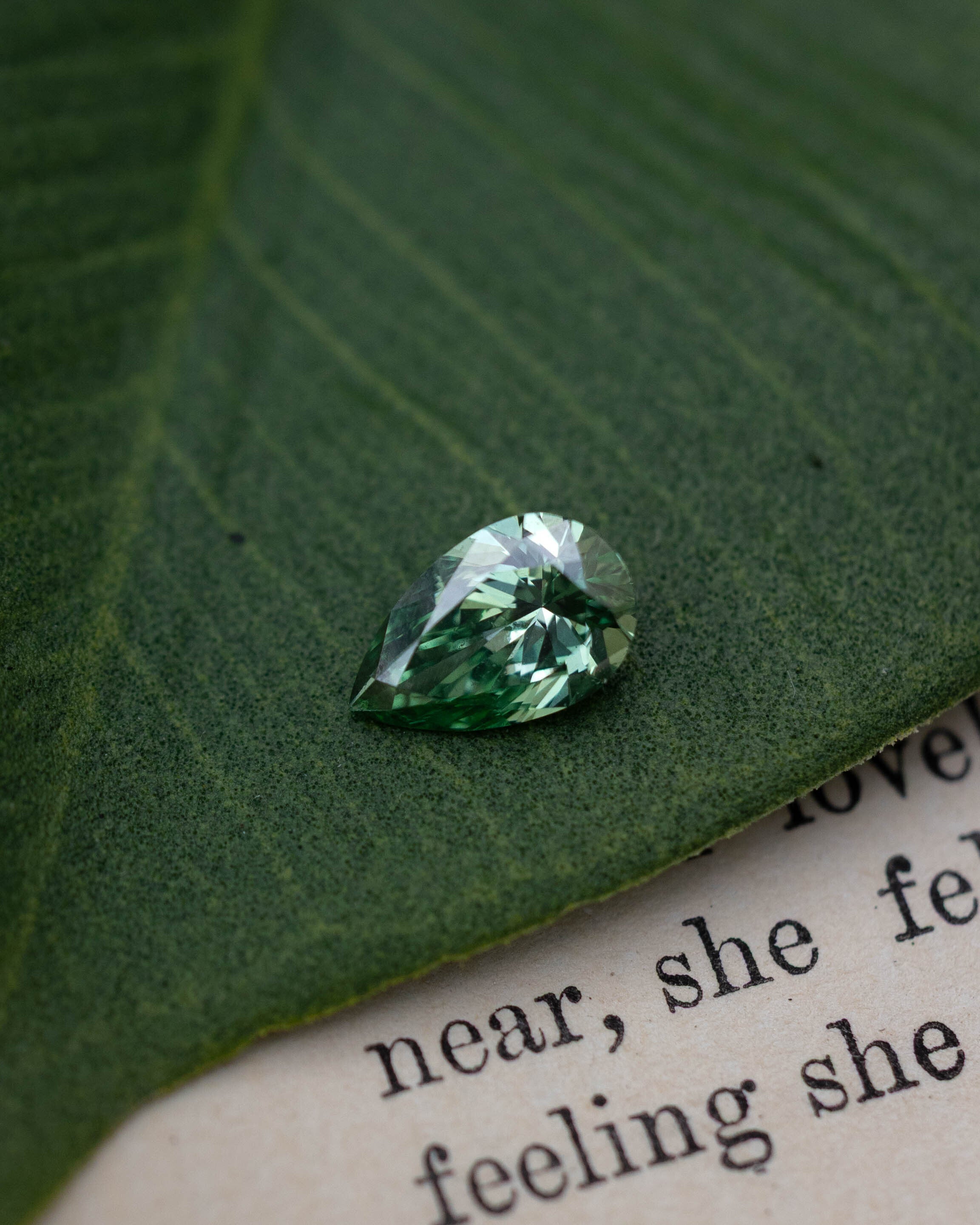 Green lab diamond sitting on top of a green leaf and piece of paper