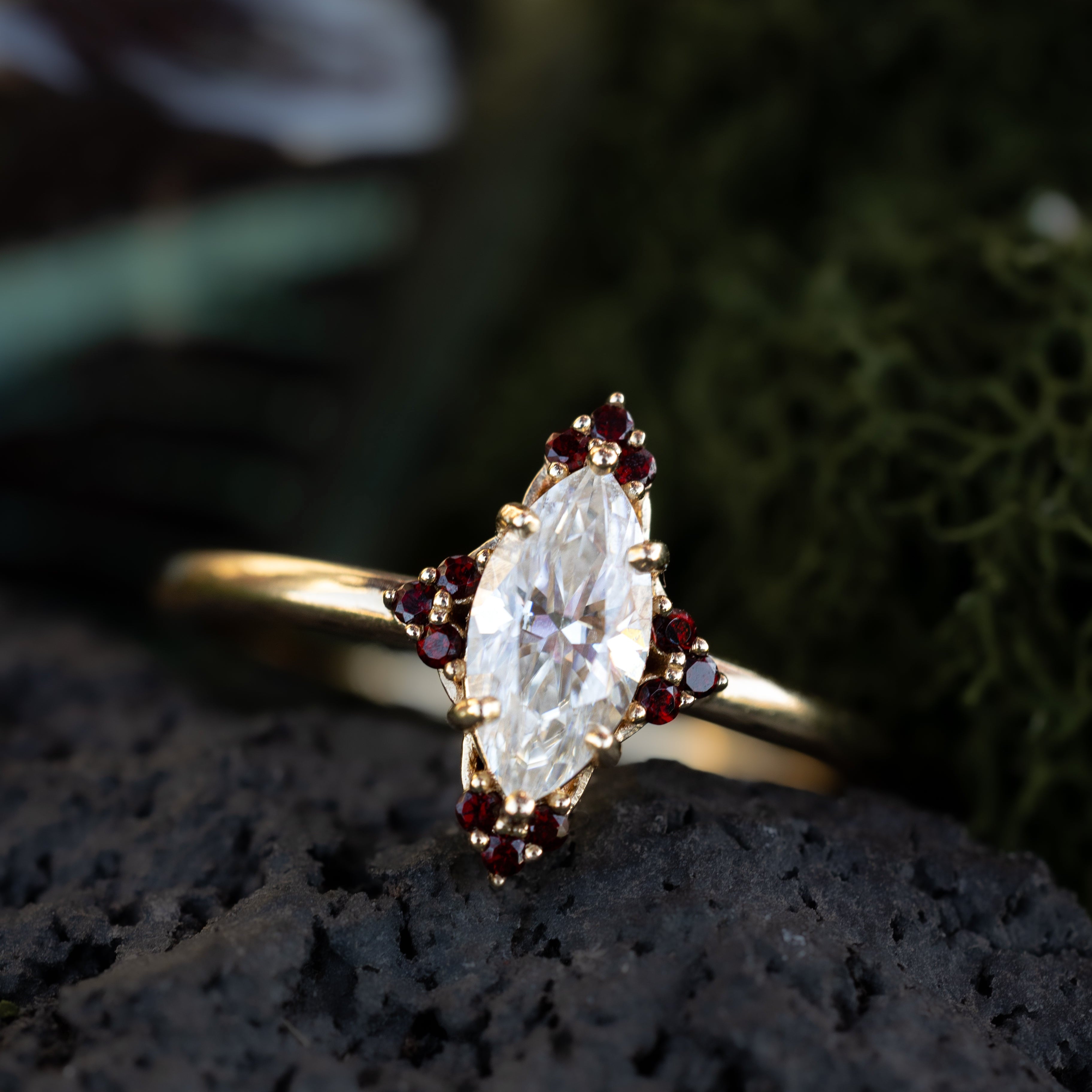 Gold ring with a large moissanite and garnet accents on a dark surface