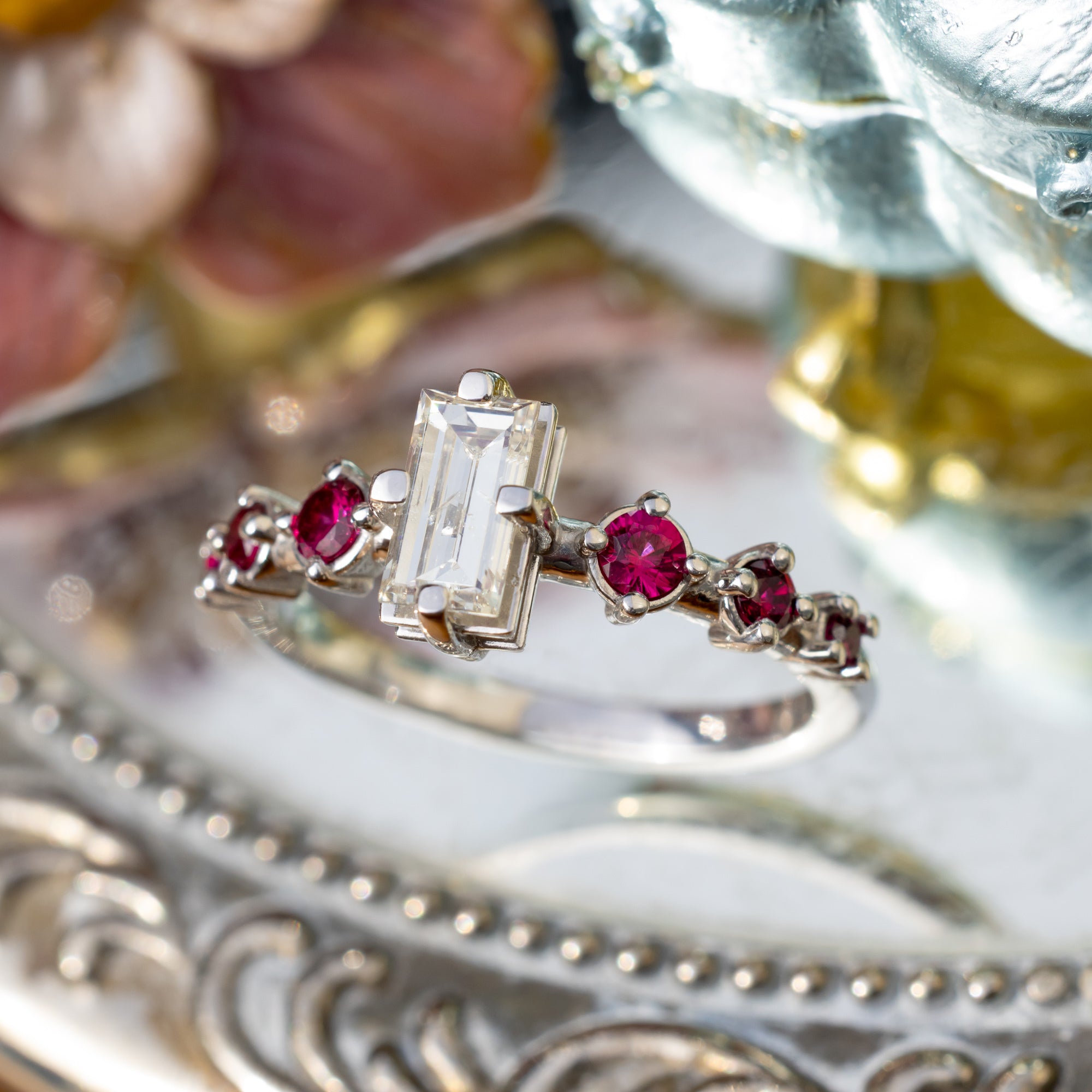 Elegant ring with emerald-cut champagne diamonds and ruby accents on a decorative surface