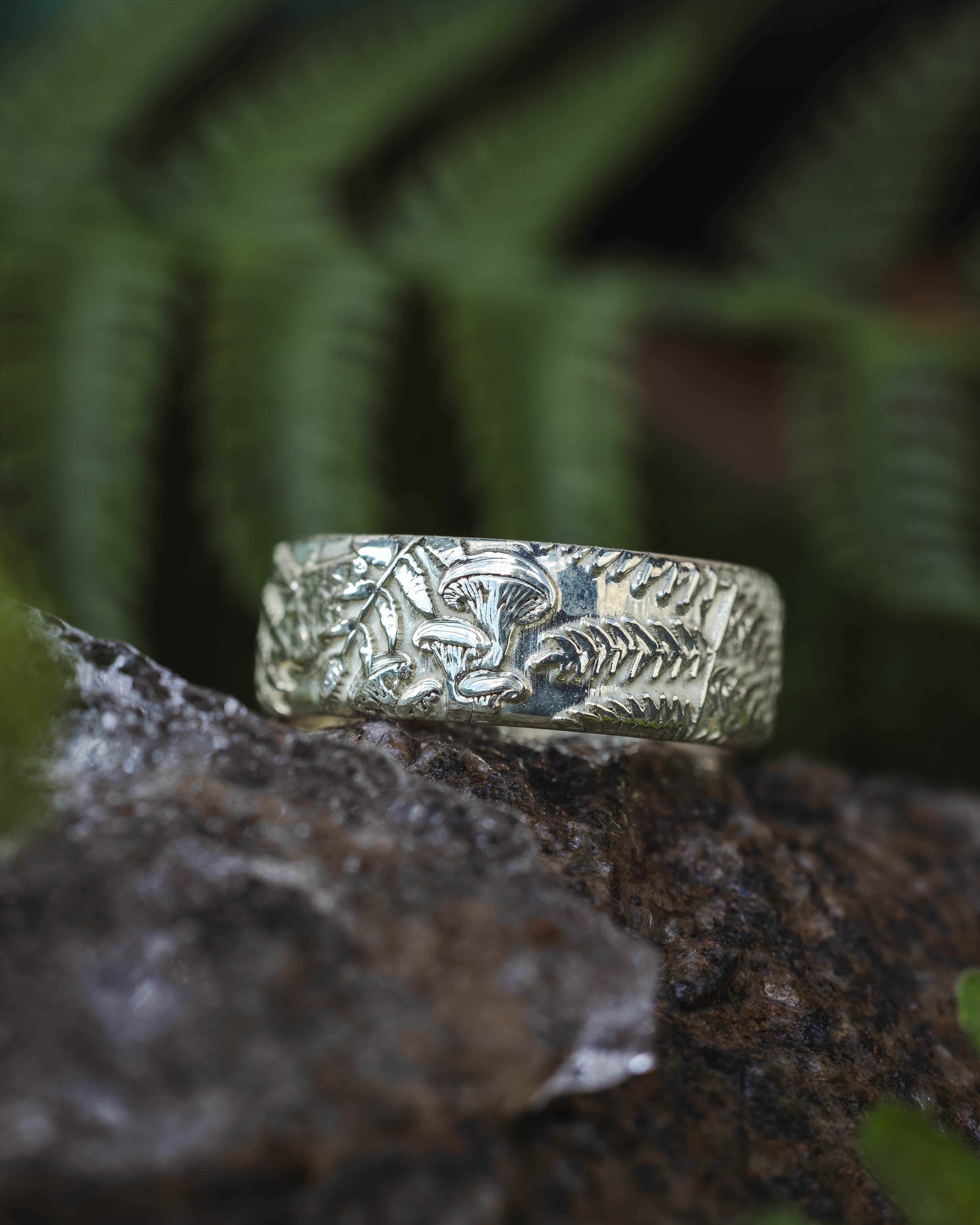 Green gold ring with intricate design on a rock with ferns in the background