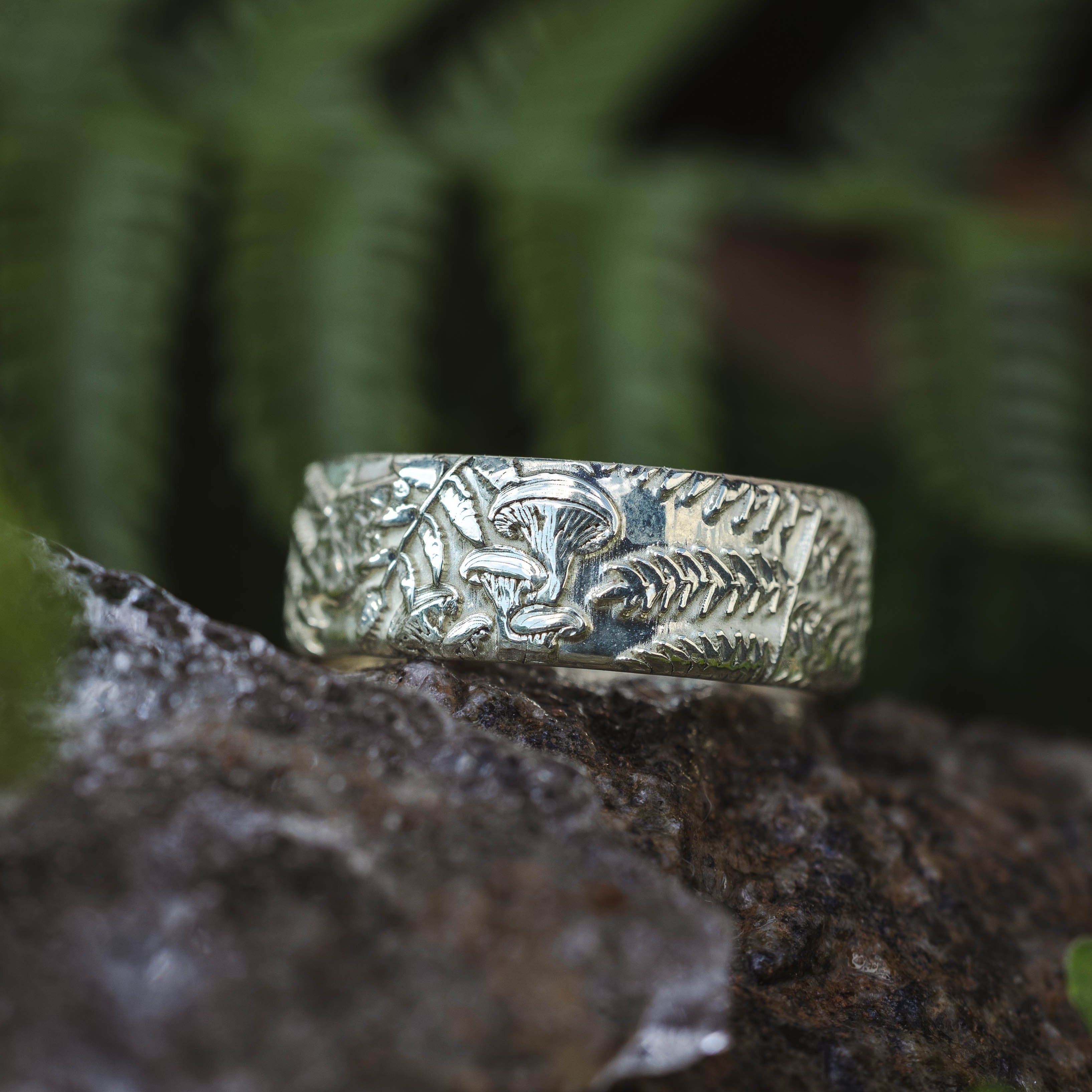 Green gold ring with intricate design on a rock with ferns in the background
