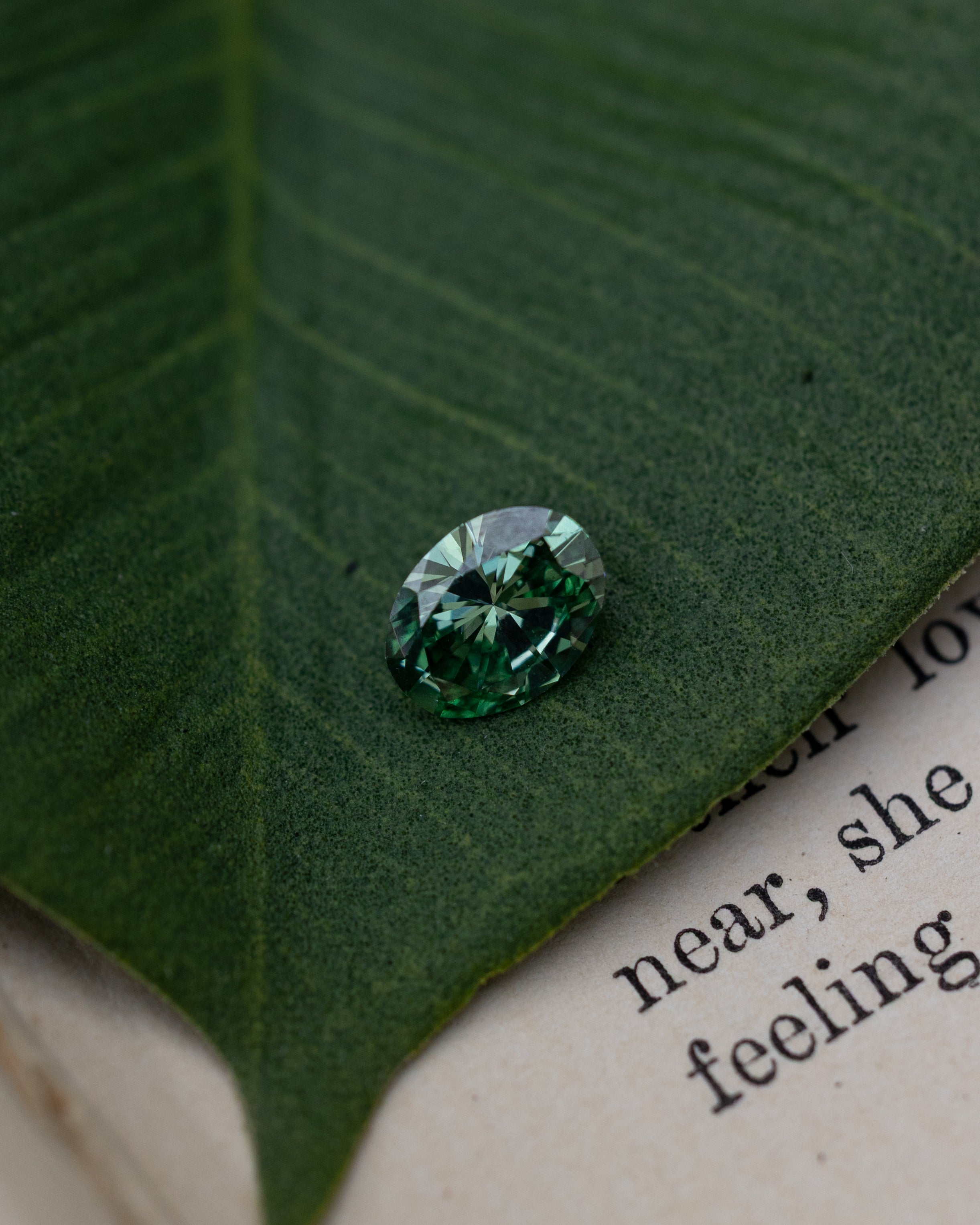 Green lab diamond sitting on top of a green leaf and piece of paper