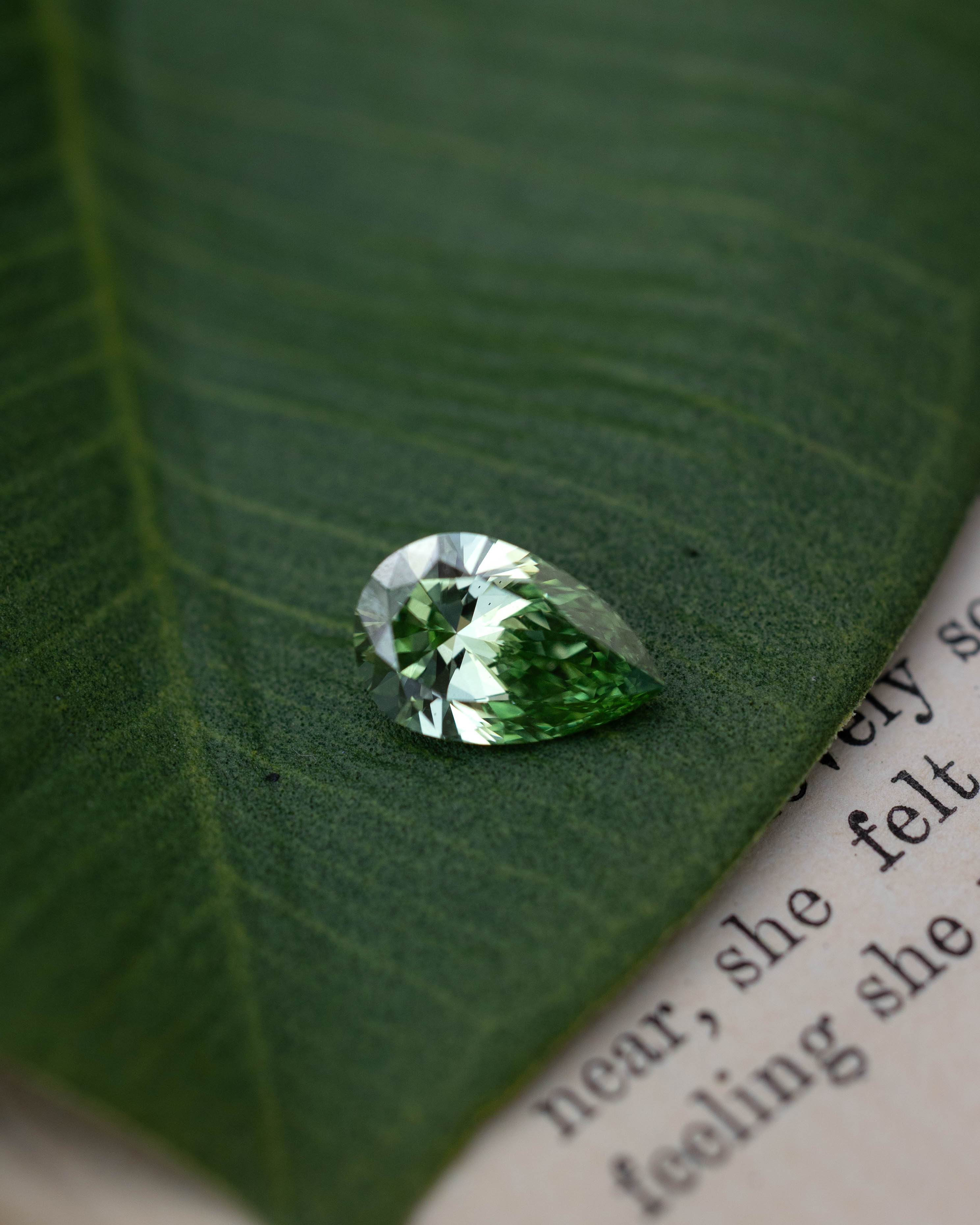 Green lab diamond sitting on top of a green leaf and piece of paper