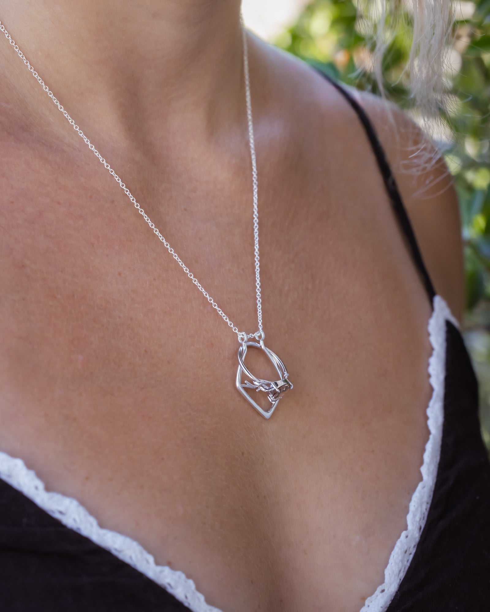 A silver necklace with an antler design on a model's neck, wearing a black and white top