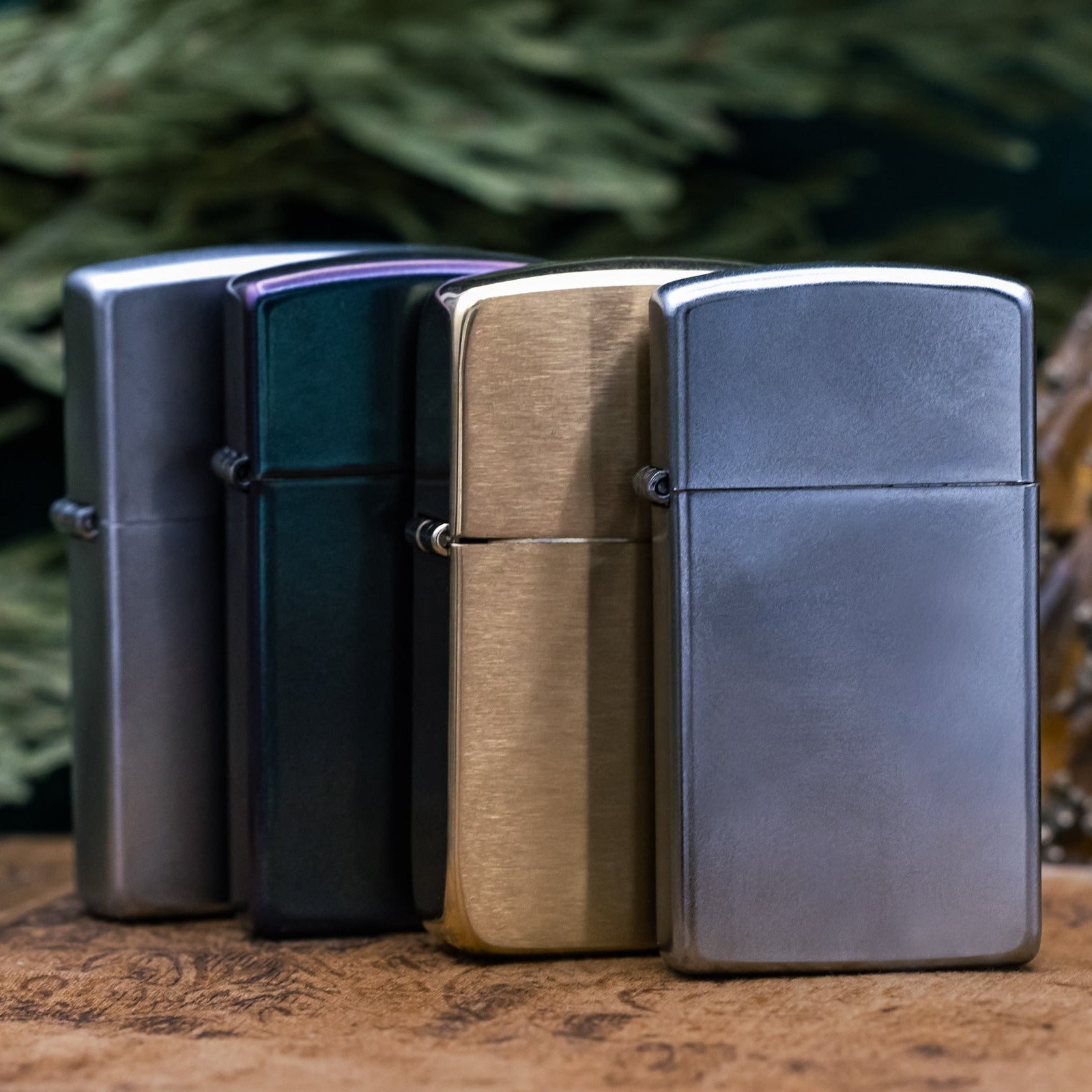 Four Zippo lighters in different finishes on a wooden surface with a blurred natural background