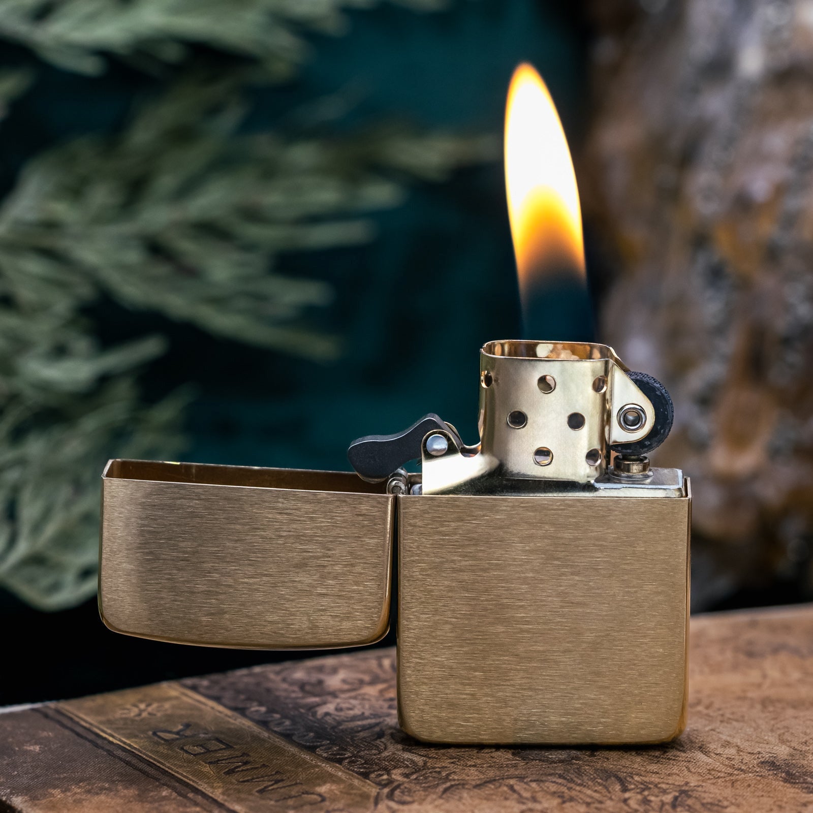 Brass Zippo lighter with flame on a wooden surface with a blurred natural background