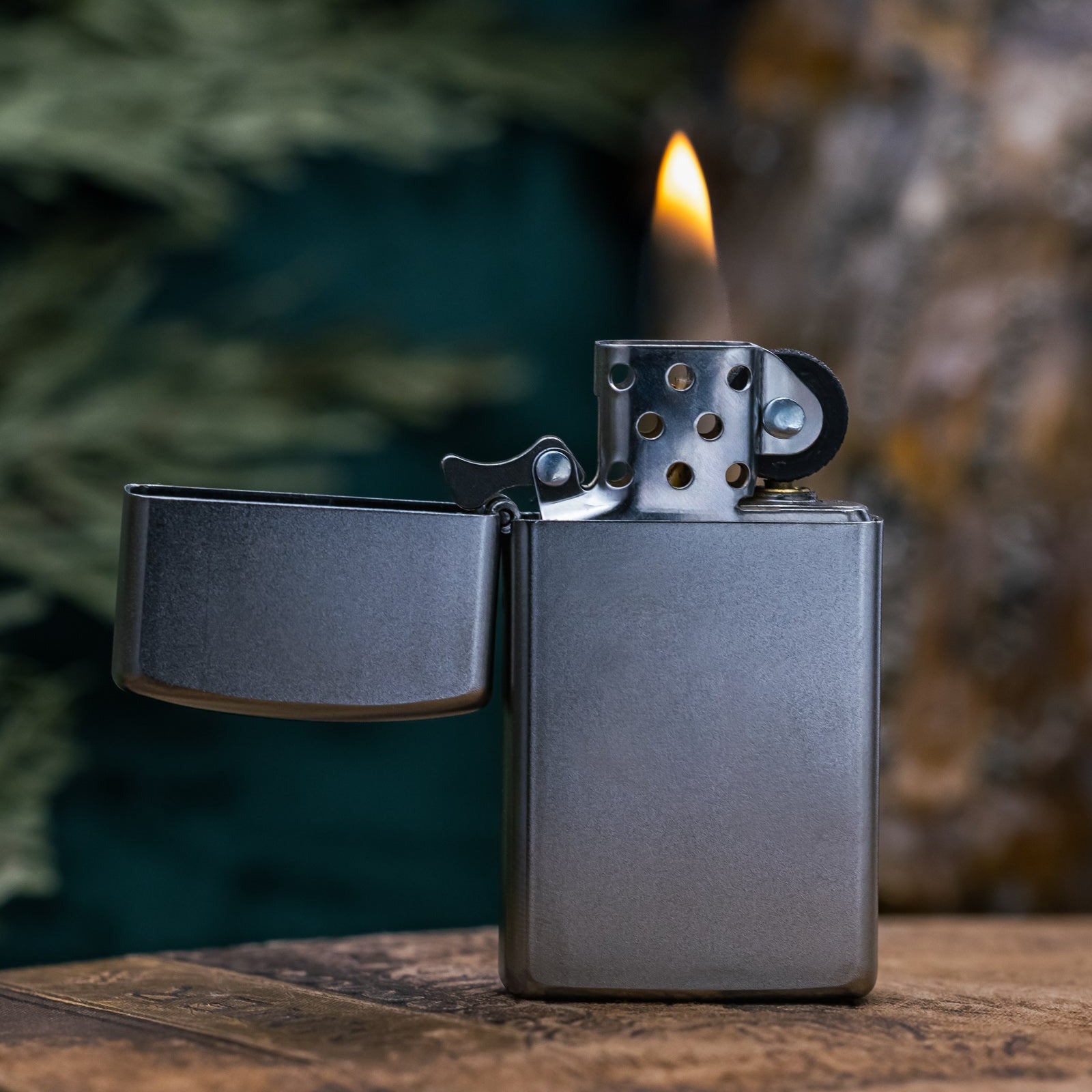 Zippo lighter with flame on a wooden surface with a blurred natural background