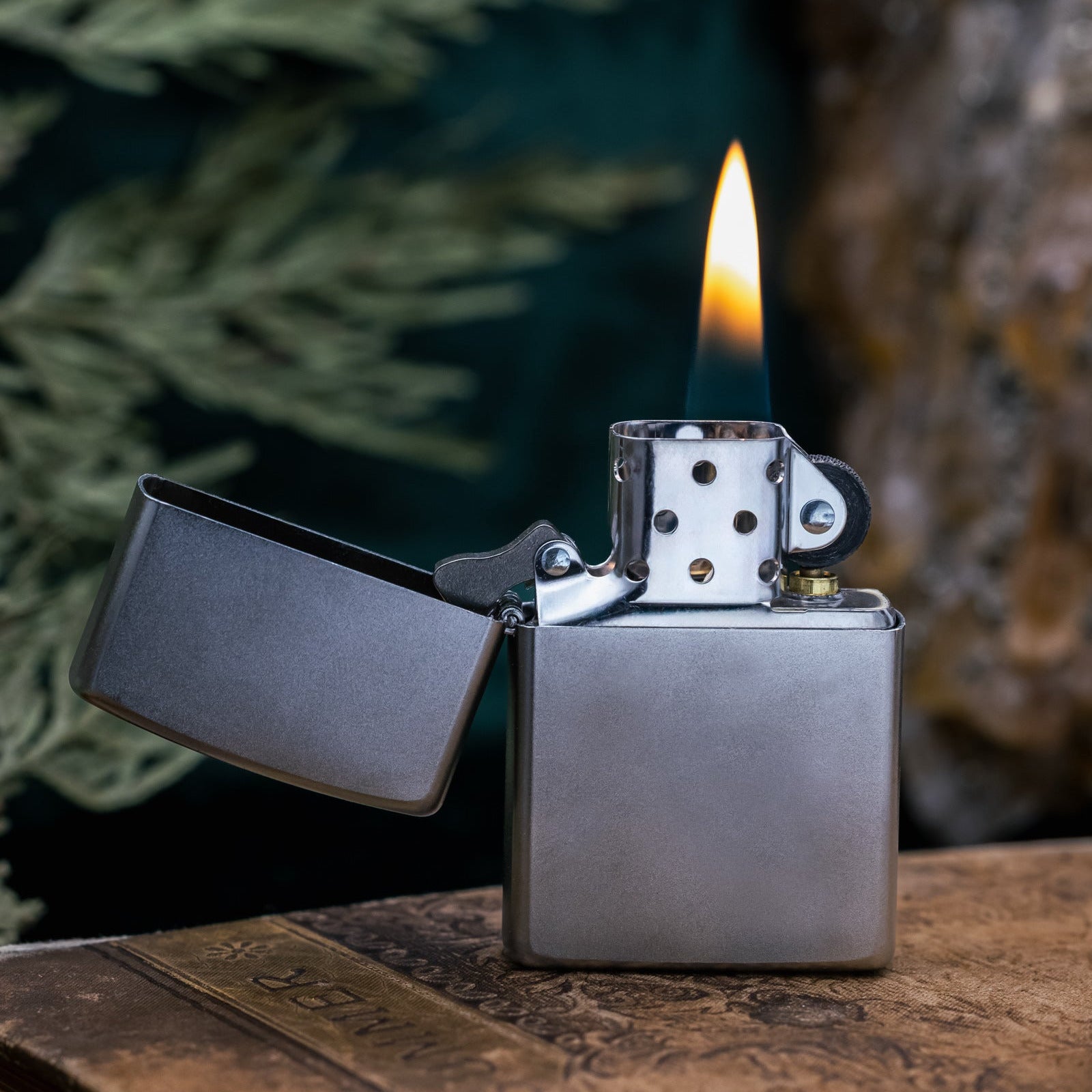 Zippo lighter with flame on a wooden surface with a blurred natural background