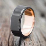Shown here is "Vulcan", a handcrafted men's wedding ring, shown here featuring a black zirconium band with a rose gold lining, upright facing left. Additional inlay options are available upon request.