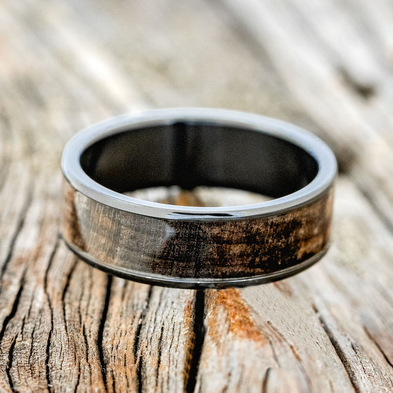 Shown here is "Rainier", a custom, handcrafted men's wedding ring featuring dark maple wood inlay, shown here on a fire-treated black zirconium band, laying flat. Additional inlay options are available upon request.