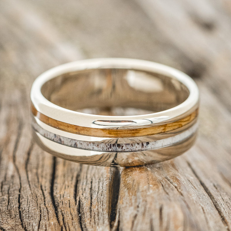 Shown here is "Cosmo", a custom, handcrafted men's wedding ring featuring whiskey barrel oak and antler inlays, laying flat. Additional inlay options are available upon request.