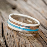 Shown here is "Cosmo", a custom, handcrafted men's wedding ring featuring 2 channels with a turquoise and a patina copper inlay, tilted left. Additional inlay options are available upon request.