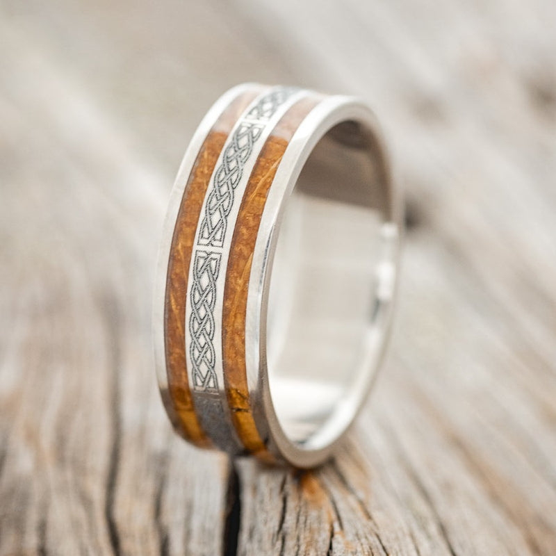 Shown here is "Ryder", a custom engraved Celtic sailor's knot-patterned men's wedding ring featuring whiskey barrel inlays, upright facing left. Additional inlay options are available upon request.