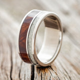 Shown here is "Raptor", a custom, handcrafted men's wedding ring featuring granite and redwood inlays on a titanium band, upright facing left. Additional inlay options are available upon request.