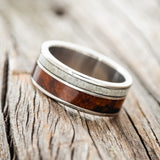 Shown here is "Raptor", a custom, handcrafted men's wedding ring featuring granite and redwood inlays on a titanium band, tilted left. Additional inlay options are available upon request.