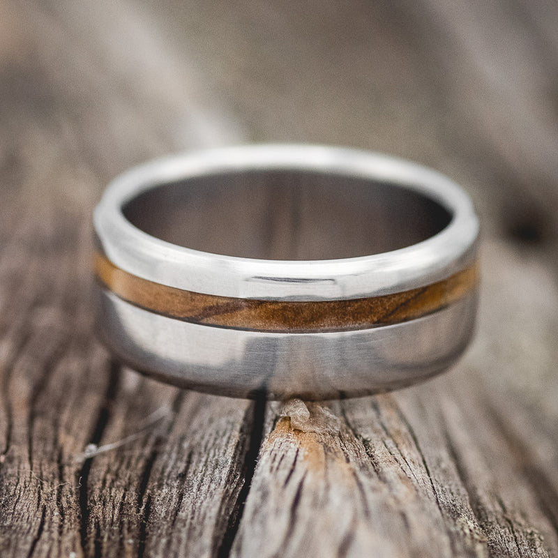 Shown here is "Vertigo", a custom, handcrafted men's wedding ring featuring a whiskey barrel inlay, laying flat. Additional inlay options are available upon request.