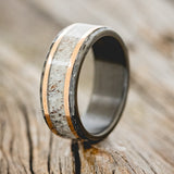 Shown here is "Hollis", a custom, handcrafted men's wedding ring featuring an elk antler & 14K rose gold inlays with a hammered, fire-treated black zirconium band, upright facing left. Additional inlay options are available upon request.