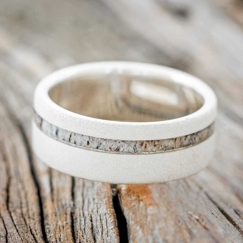 Shown here is "Vertigo", a custom, handcrafted men's wedding ring featuring an antler inlay with a sandblasted finish, laying flat. Additional inlay options are available upon request.